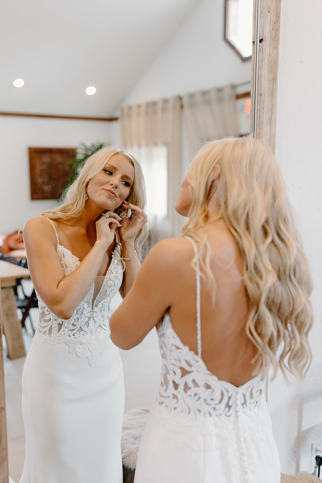 Bride puts on her earrings in front of a mirror