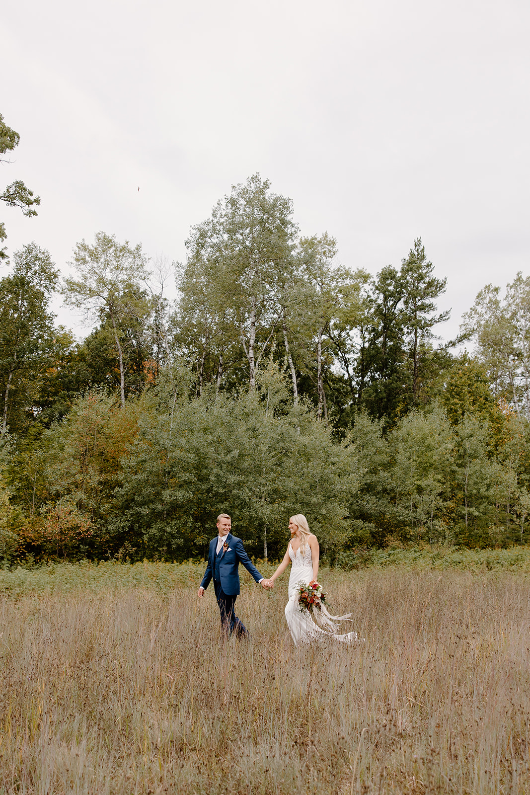 Bride and groom walk through a field of grass