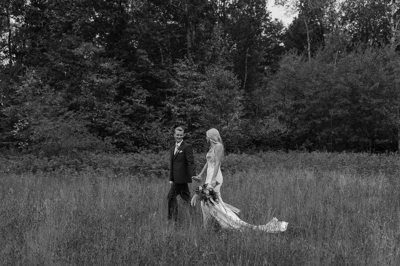 Bride and groom walk through a field of grass