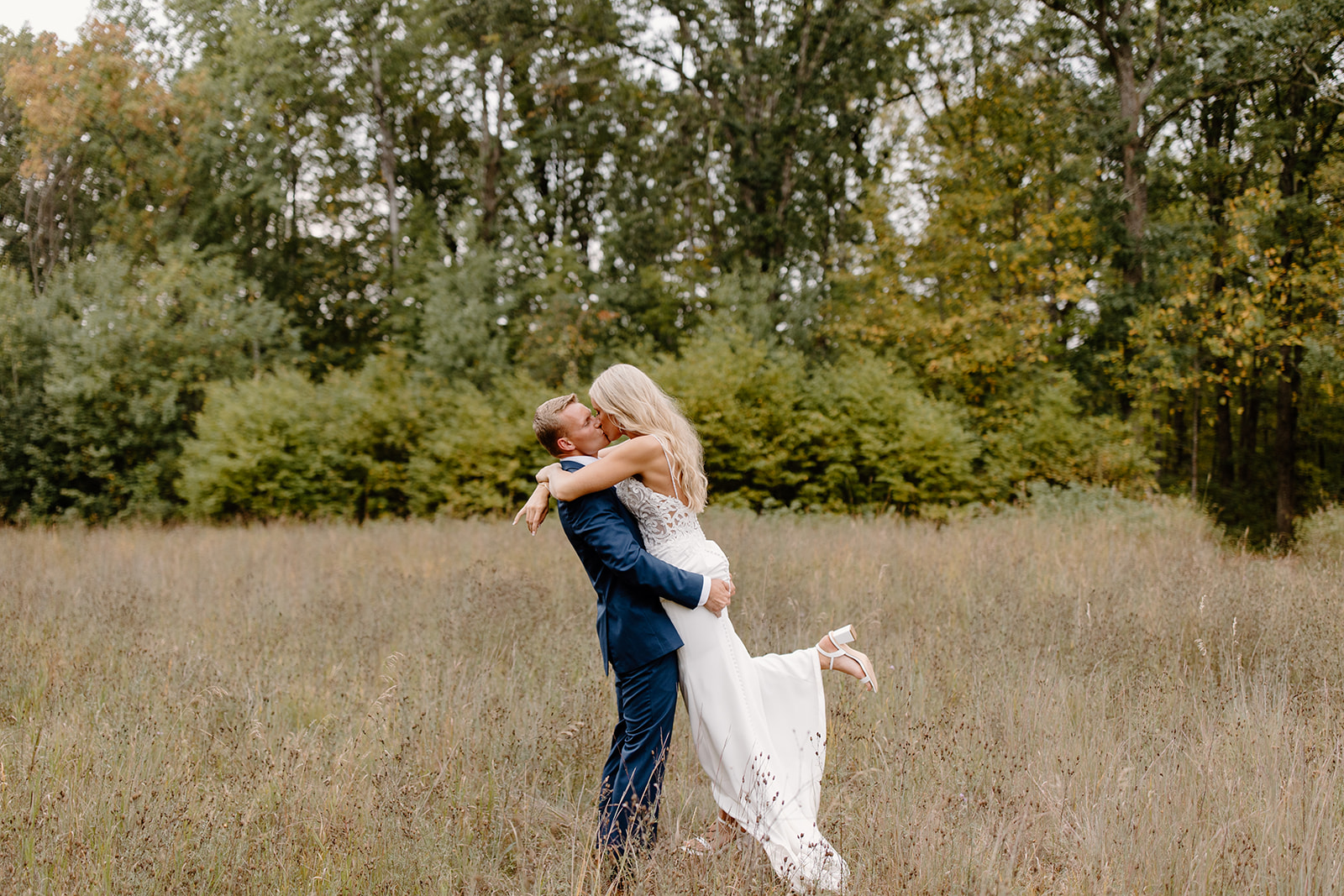 Groom holds his bride in a field of grass