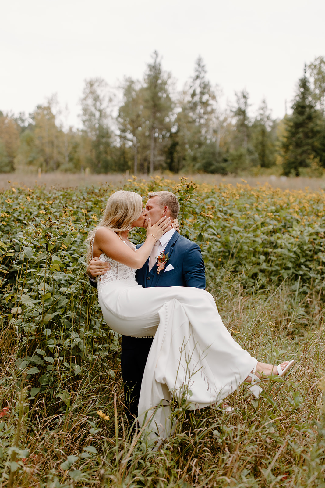 Groom holds his bride in a field of grass