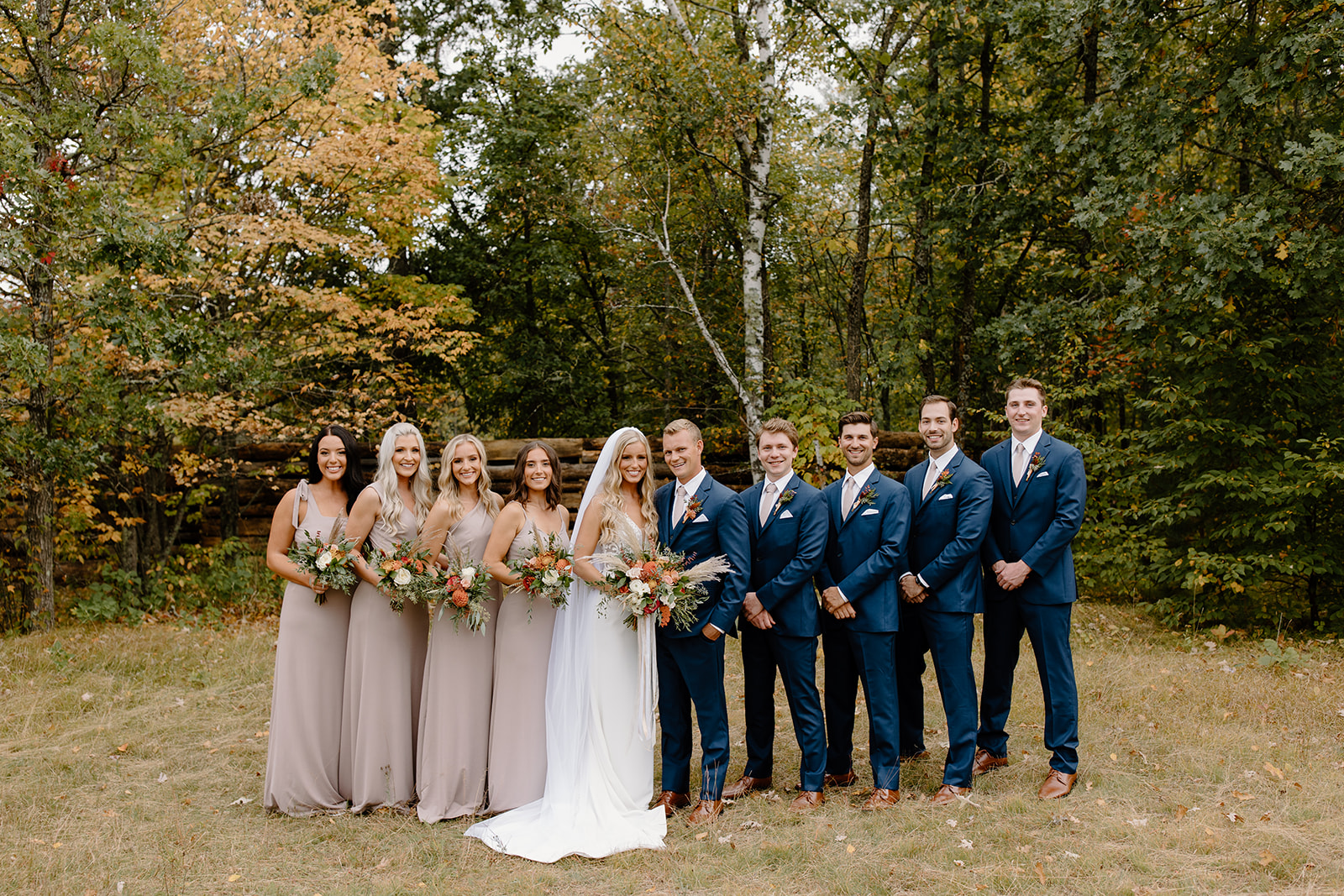 Bride and groom with their wedding party in front of trees with leaves changing color