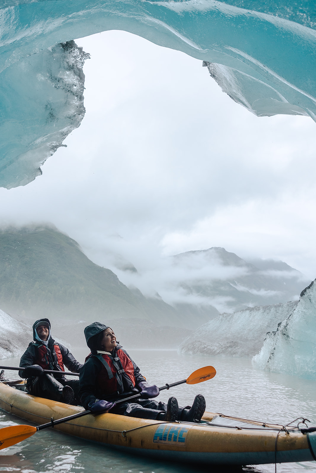 couple kayaks into ice caves in a glacier lake in alaska for their destination wedding