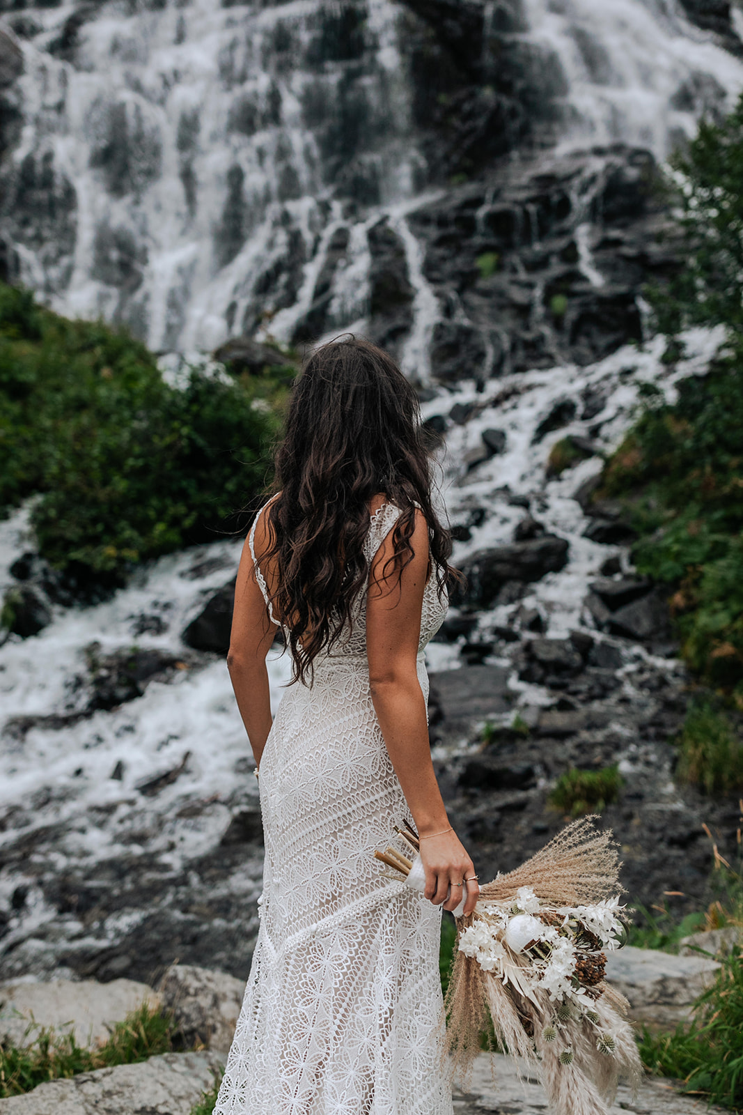 couple takes photos with a waterfall in alaska on their wedding day