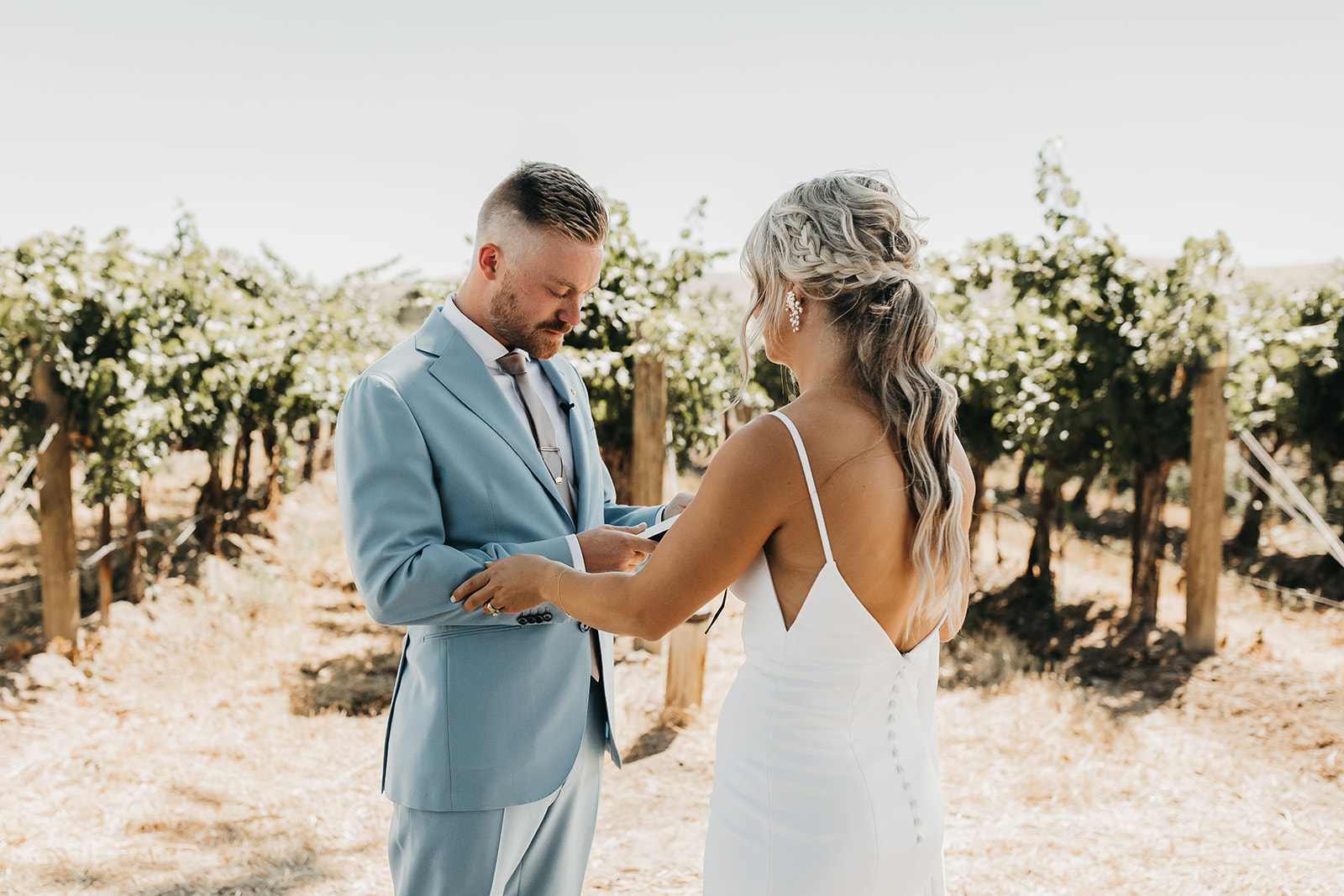 Groom reading vows to bride before wedding surrounded by beautiful rows wine vineyard in Washington