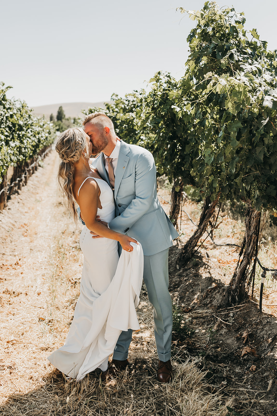 Bride and groom share kiss and special moment standing in rows of vineyard at Cooper Wine Company wedding in Washington