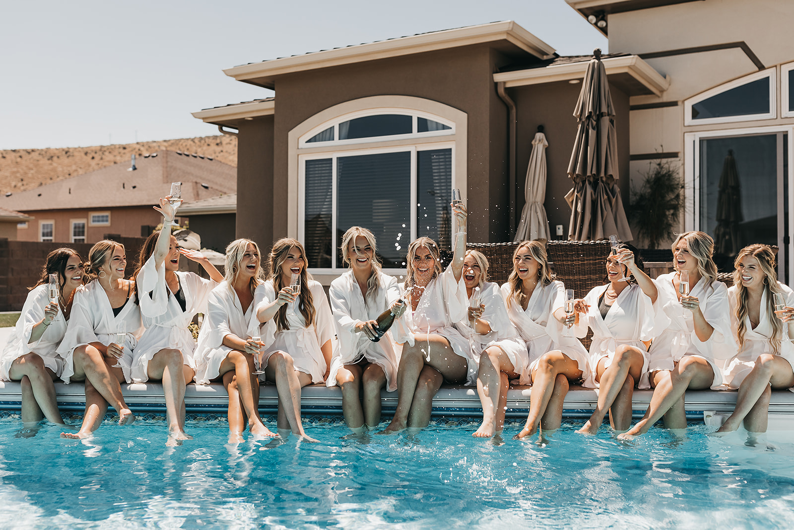 Bride and bridesmaids popping champagne by the pool before getting ready for wedding ceremony