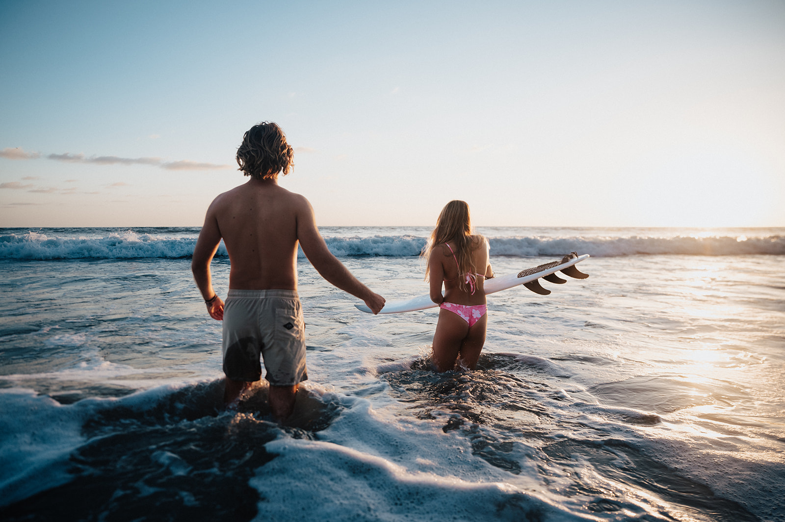 Surfer couple walks out into the ocean during sunset during the most amazing golden hour photo shoot