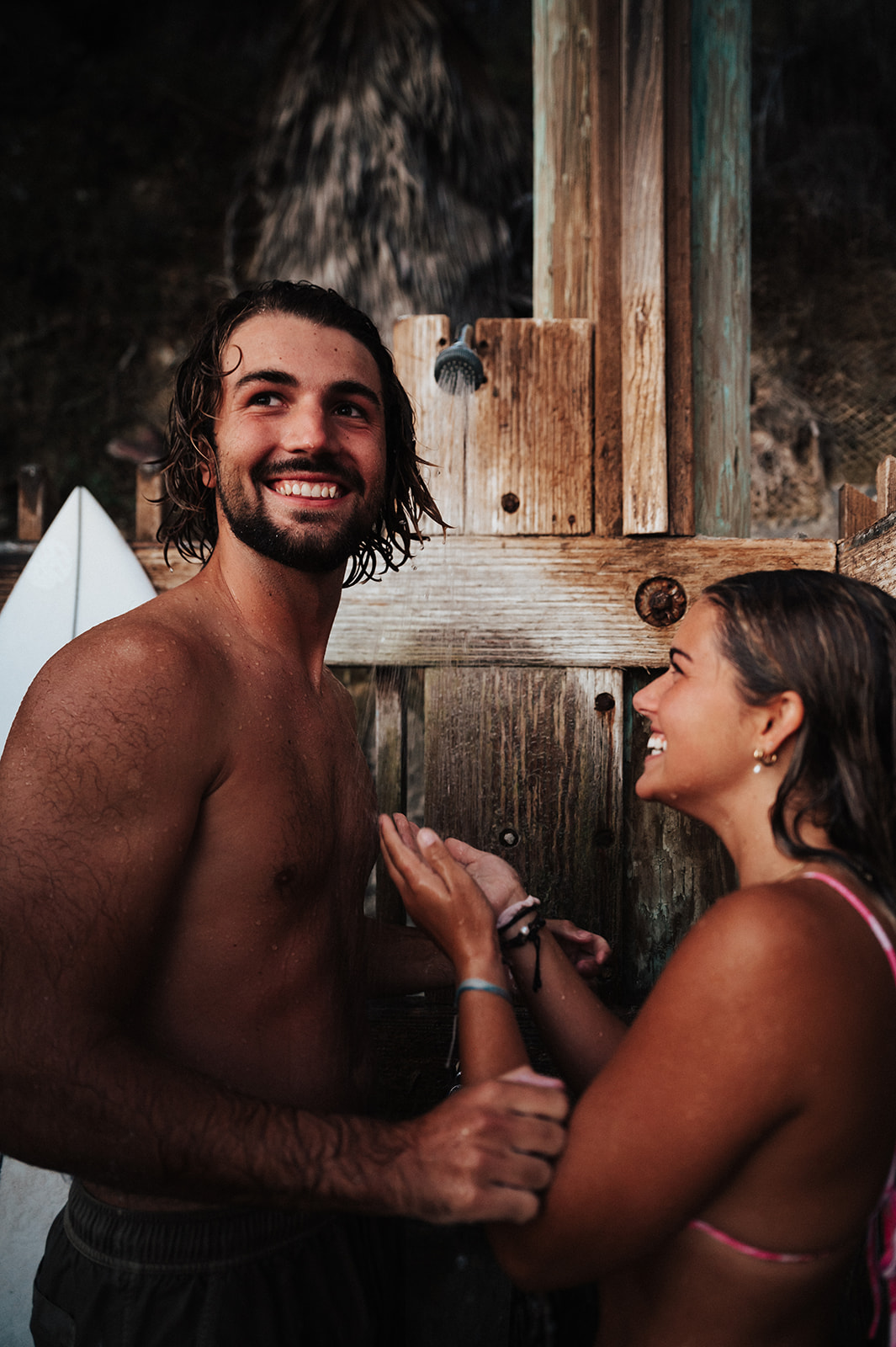 Surfer couple rinses off in an outdoor shower on the beach after a dip in the ocean for a beachy couples session