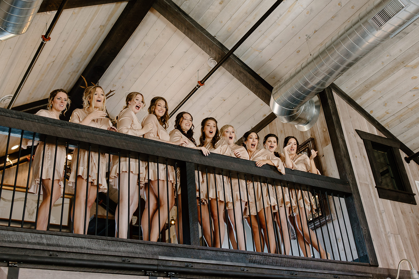 Bridesmaids on a balcony react to seeing their friend 