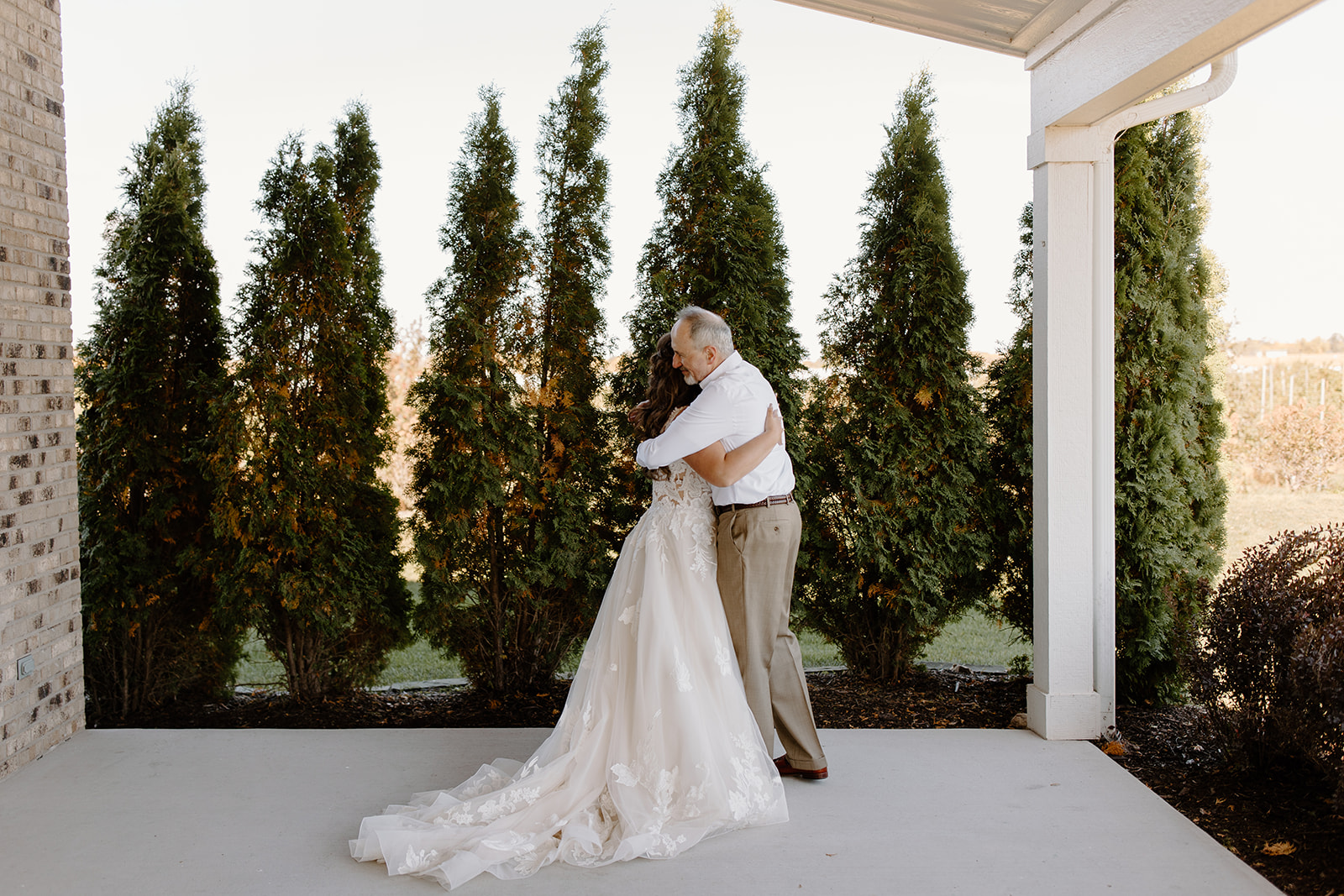 Bride hugs her father in front of trees
