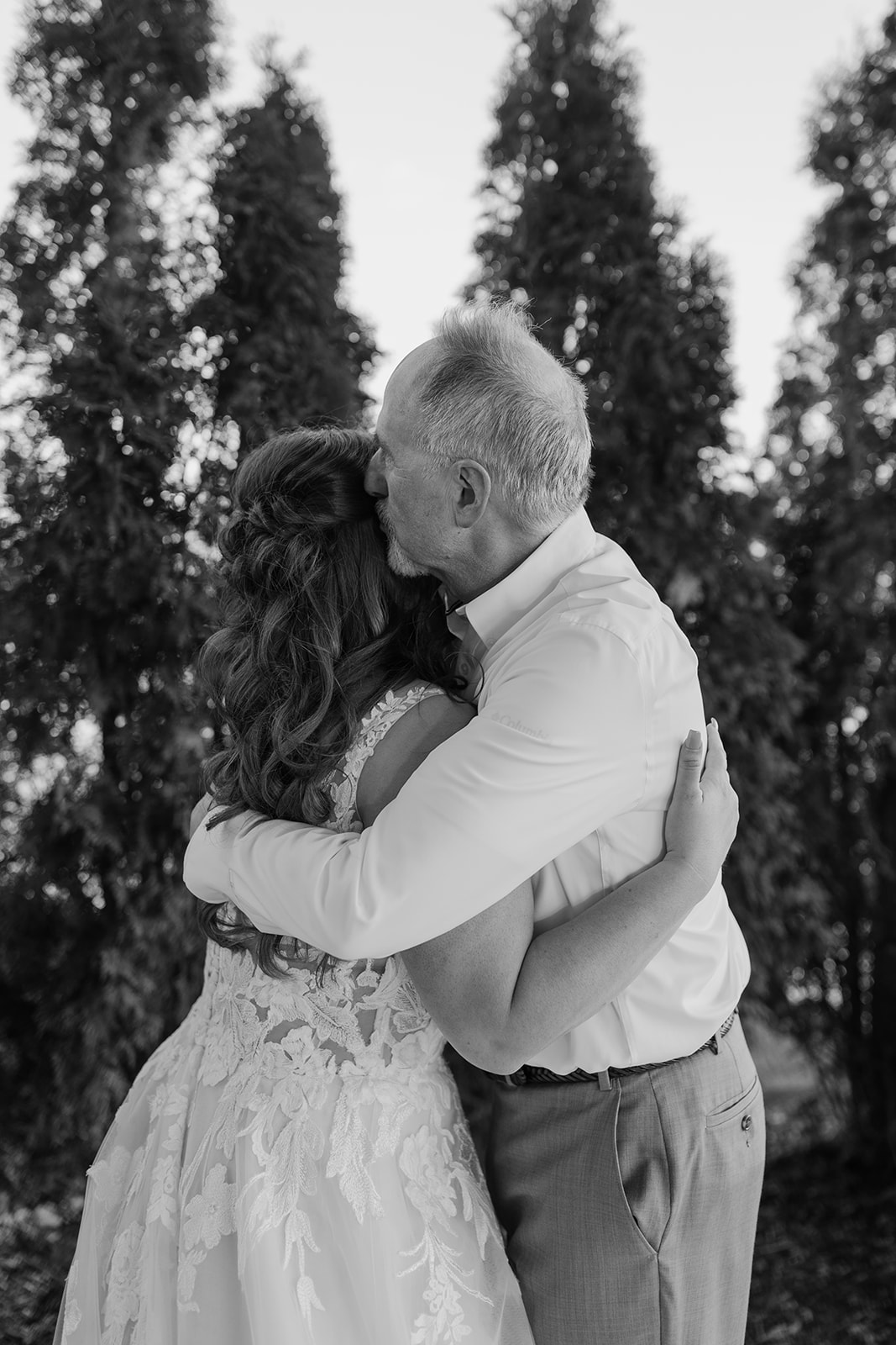 Bride hugs her father in front of trees