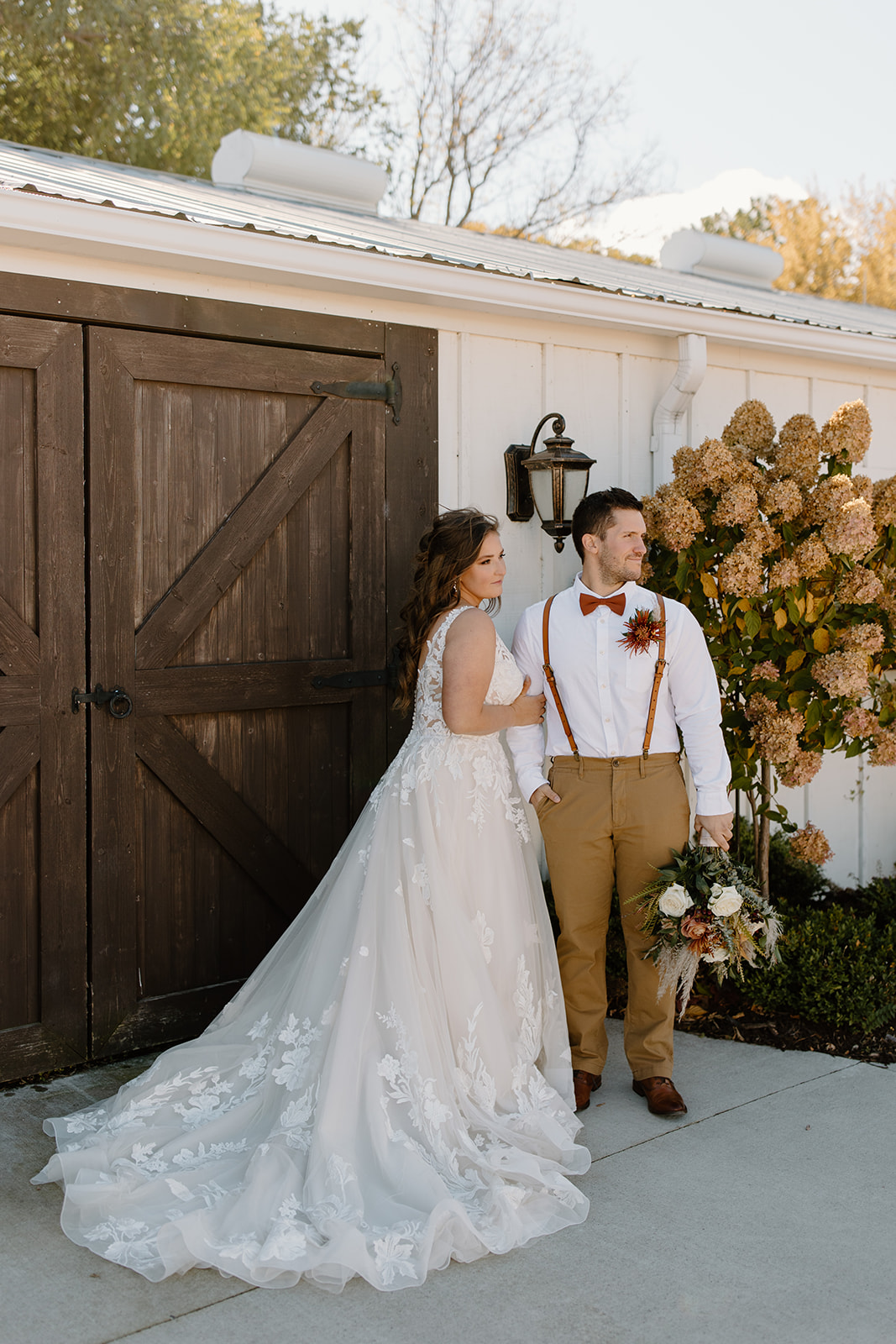 Bride and groom look away from the camera in front of a barn door