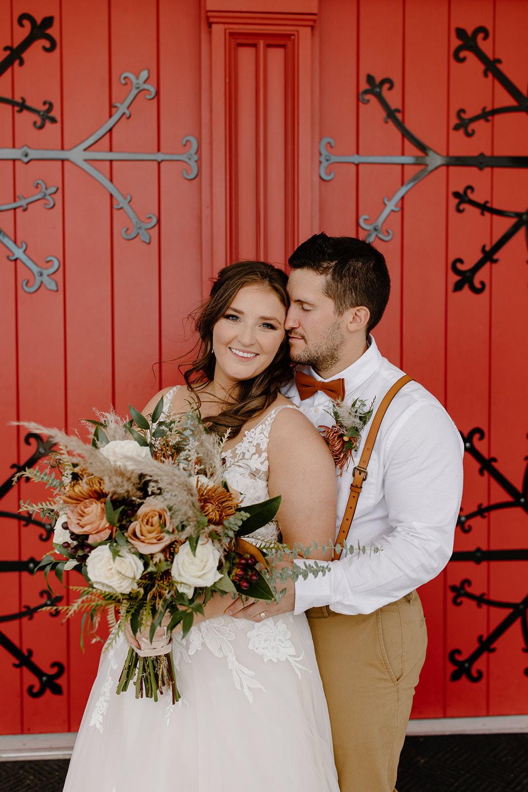 Bride and groom smile at each other in front of a big red door
