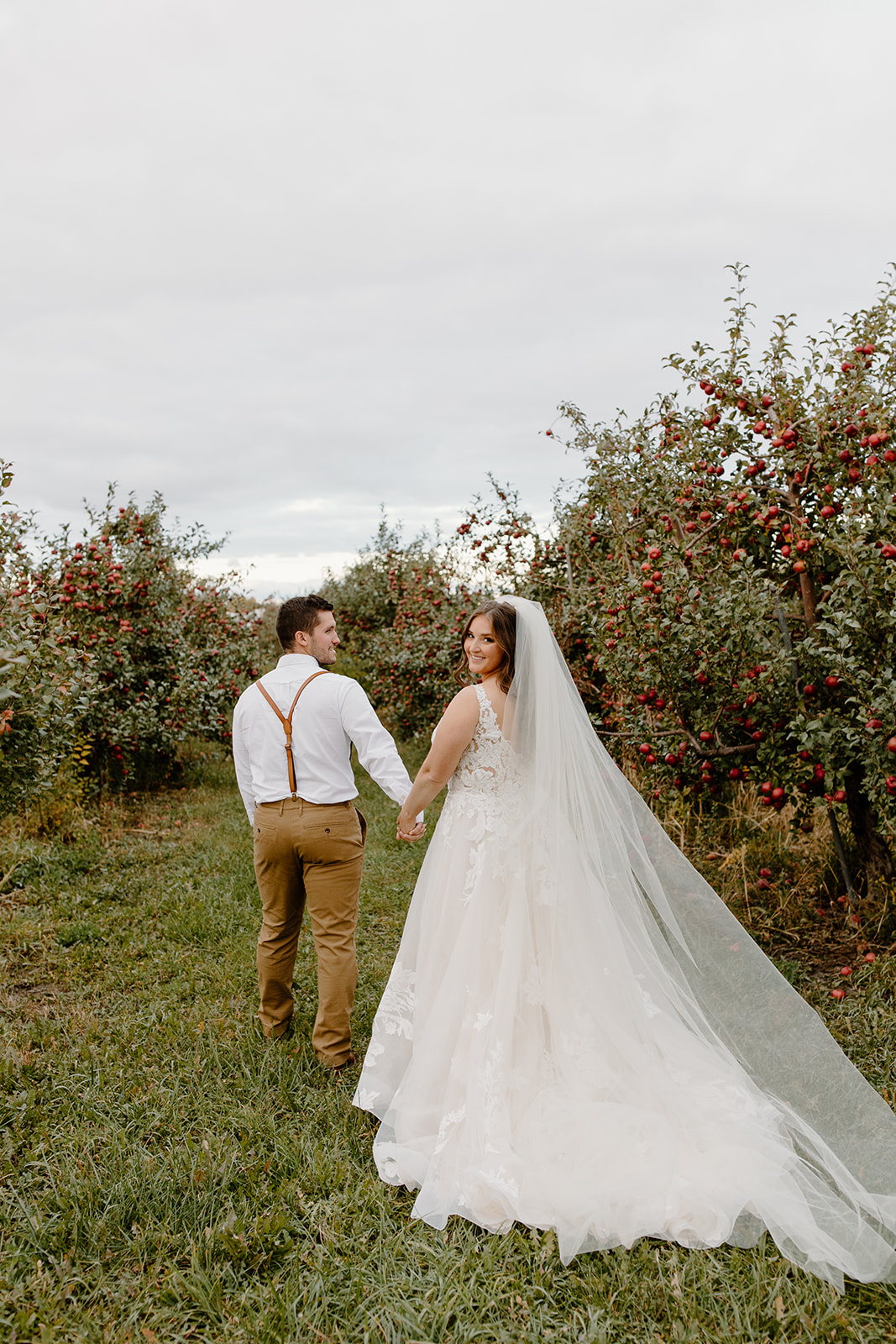 Groom leads bride between apple trees