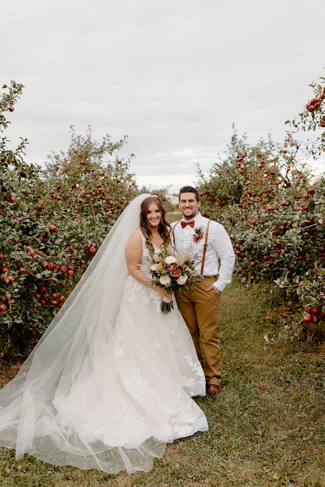Bride and groom smile between apple trees