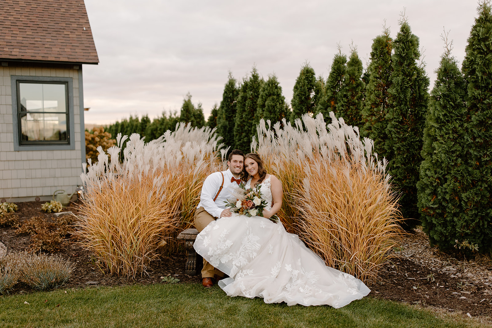 Bride and groom sit on a bench in front of pampas grass