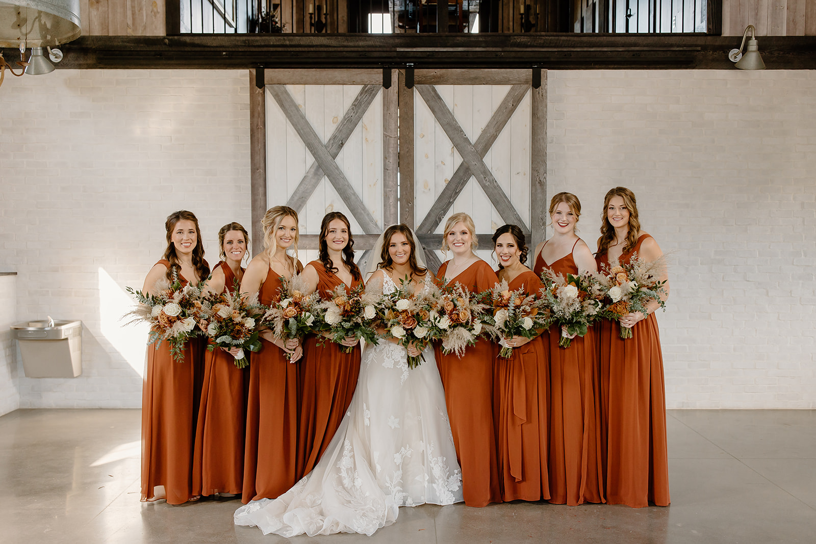 Bride and bridesmaids stand in front of a barn door