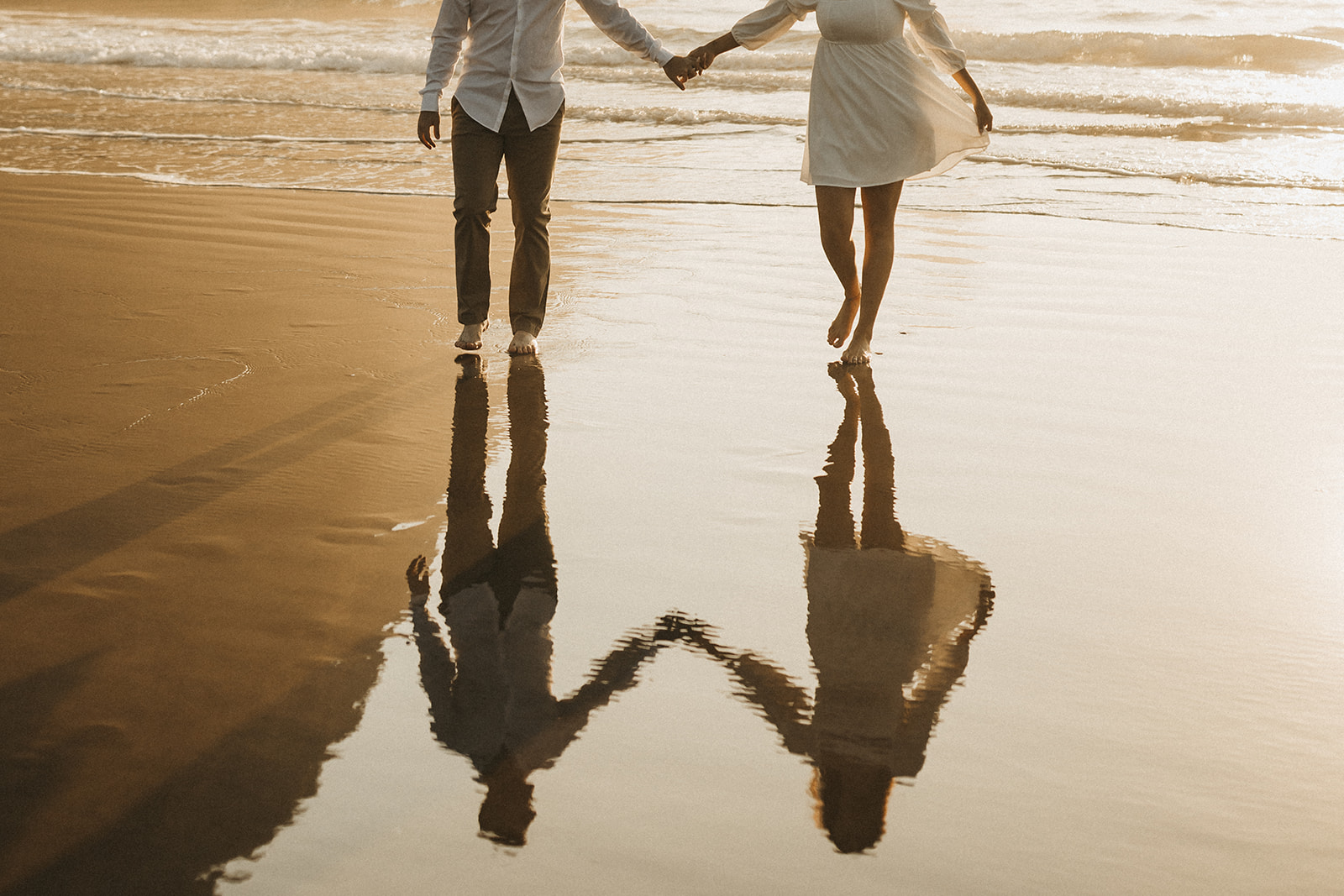reflection on sand of couple holding hands and walking on the oregon coast beach