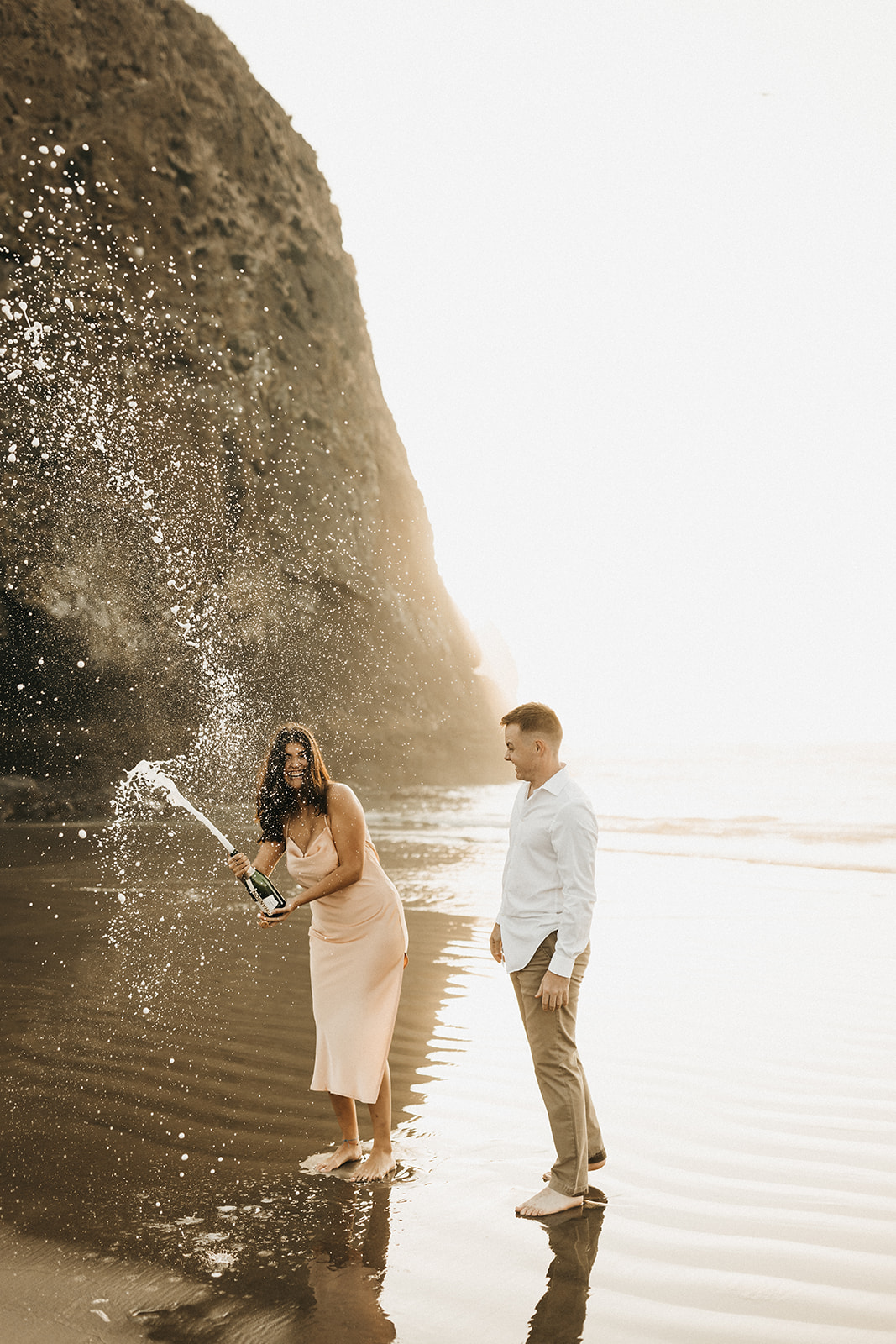 Couple popping champagne on the beach celebrating their engagement 