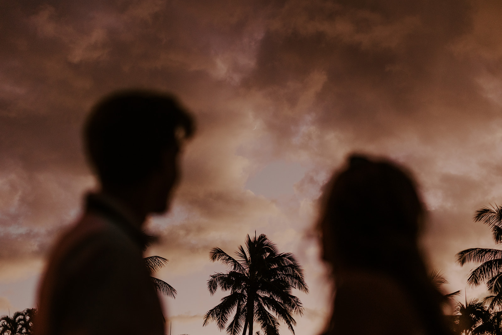 A wedding couple watches the moonrise after a sunset in Hawaii 