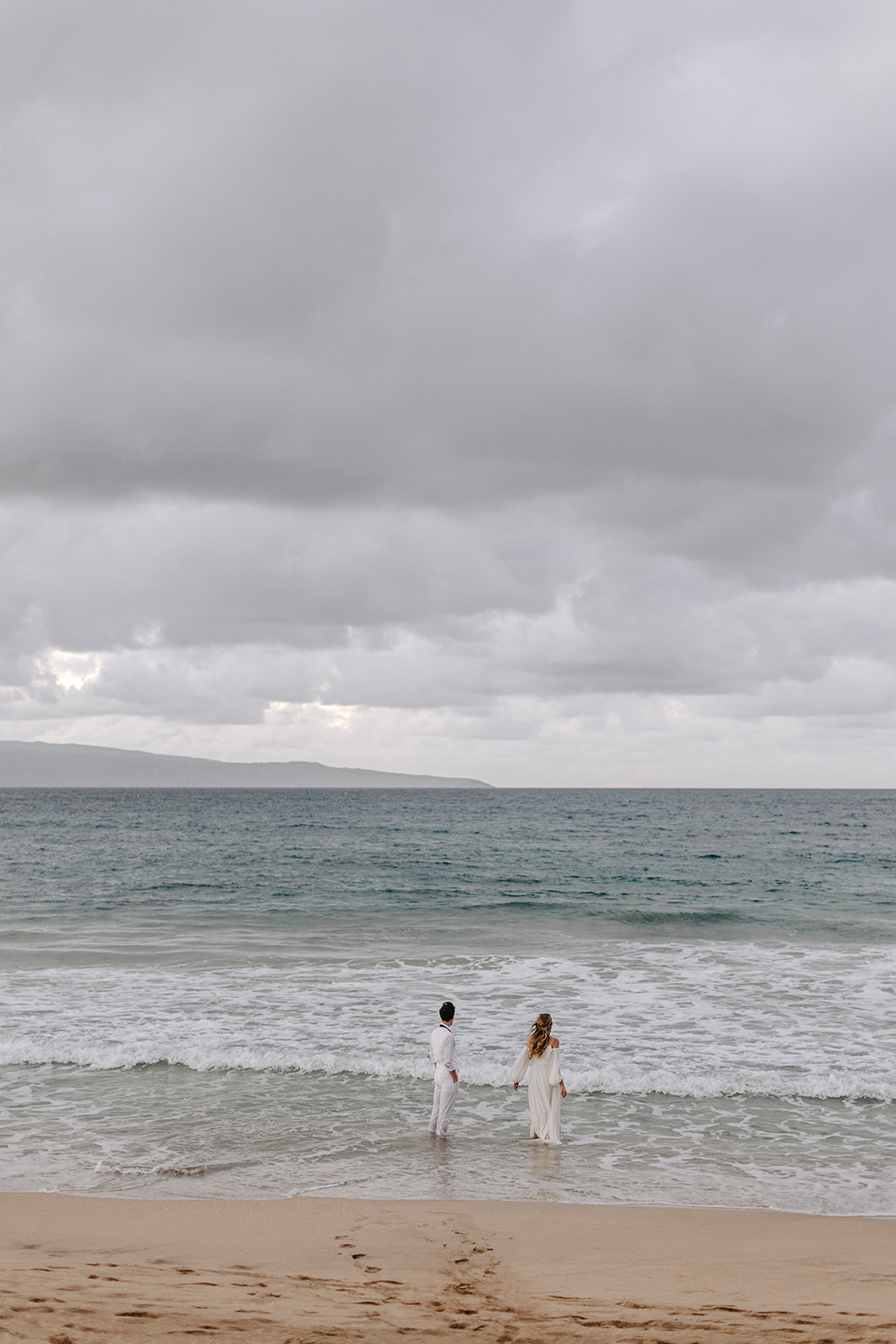 A wedding couple watches the ocean after getting married at sunset in Maui, Hawaii 