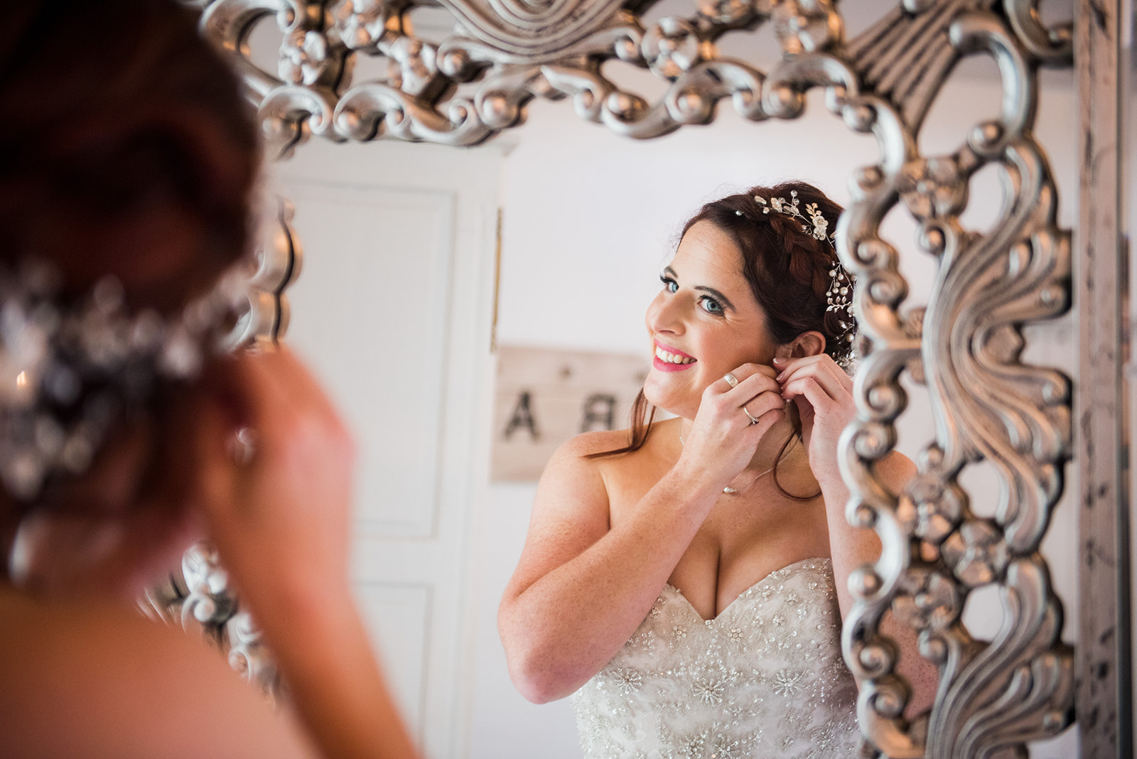 Bride looks into elegant mirror as she puts the finishing getting ready touches on.