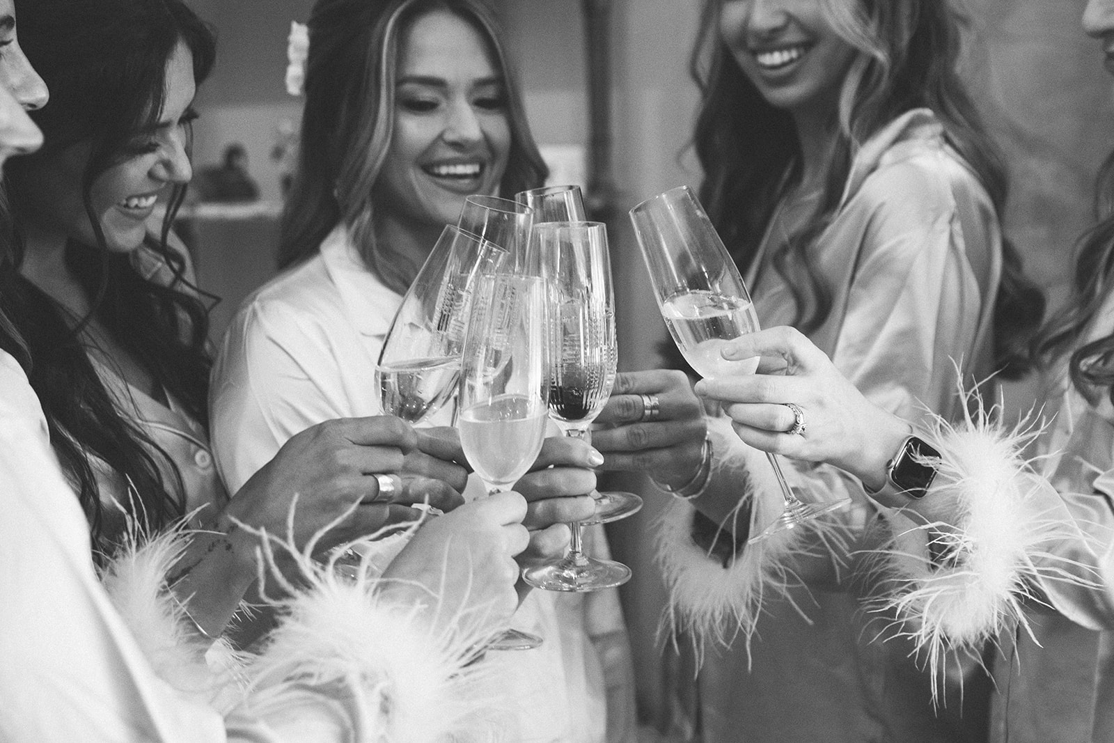 The bride and bridesmaids cheers with champagne in their matching getting ready outfits before wedding day!
