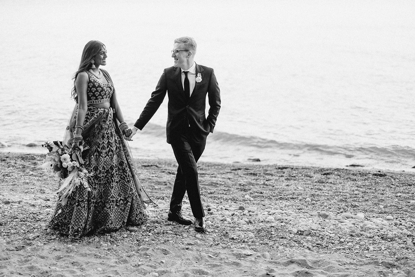 bride and groom walk alongside the coast of lake michigan on their wedding day at schlitz audubon nature center