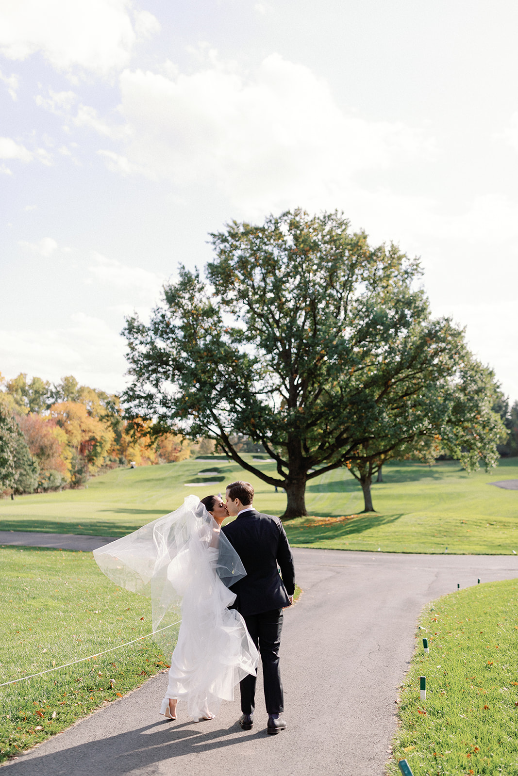 Bride and groom kissing and walking on the golf course path at Oak Hill Country Club