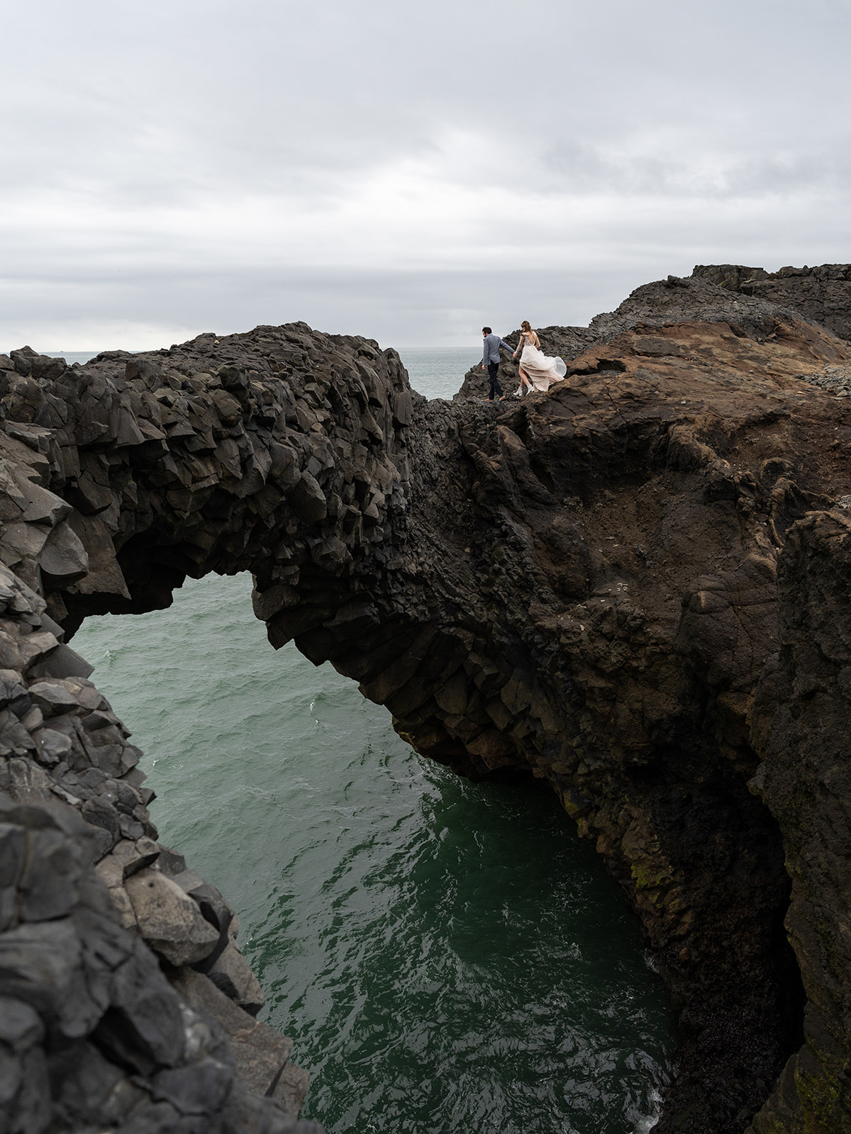 Bride and groom walking over a natural bridge during their iceland elopement 