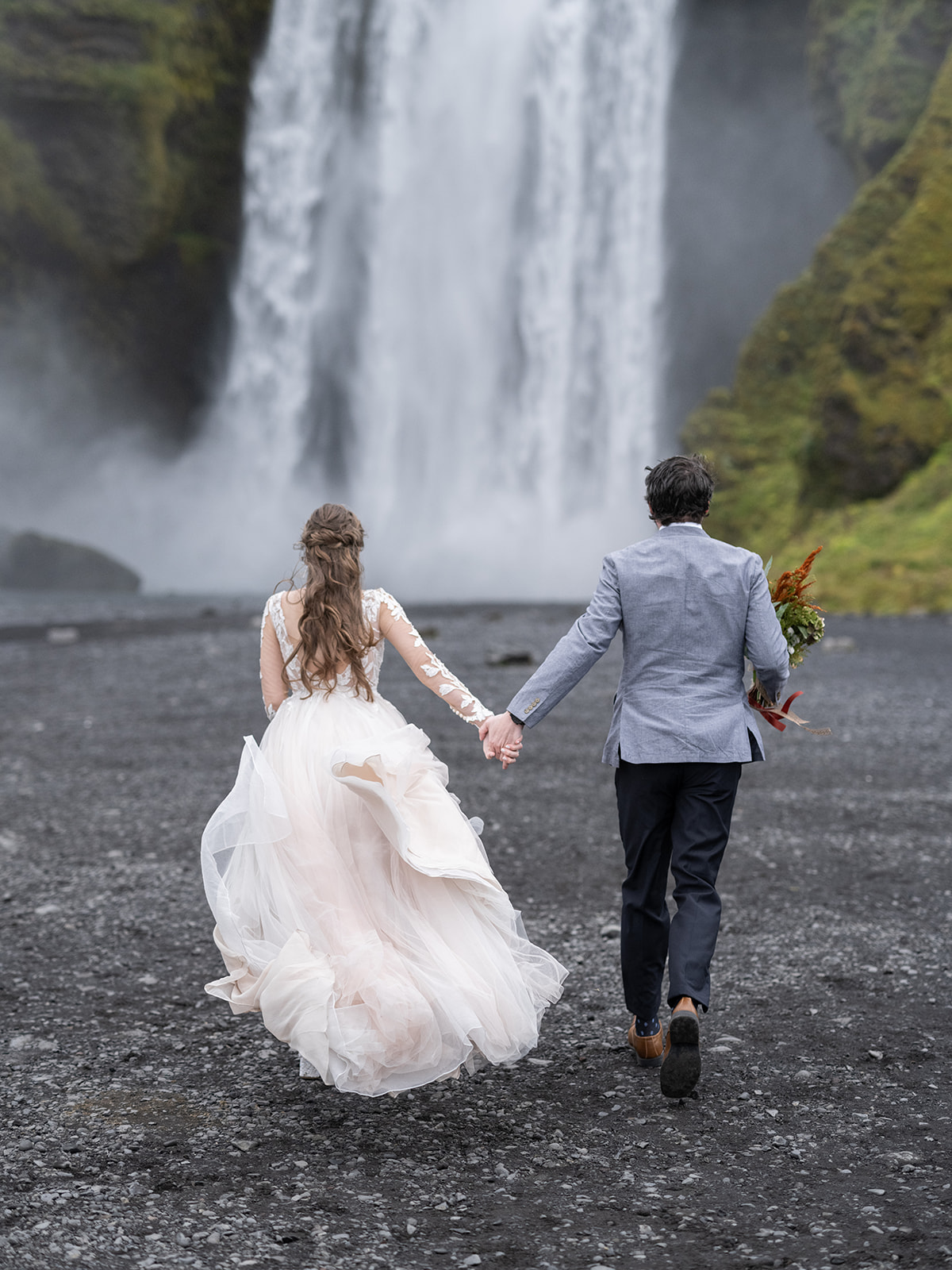 couple running towards skogafoss on thier elopement day 