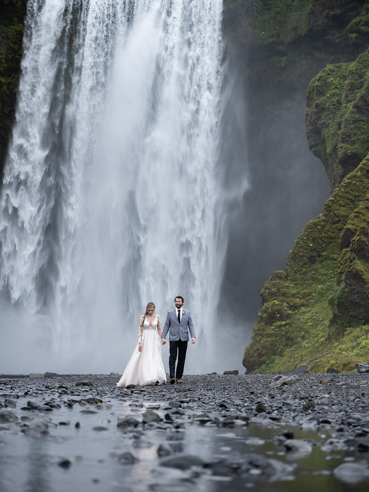 bride and groom standing for portraits in front of skogafoss iceland 