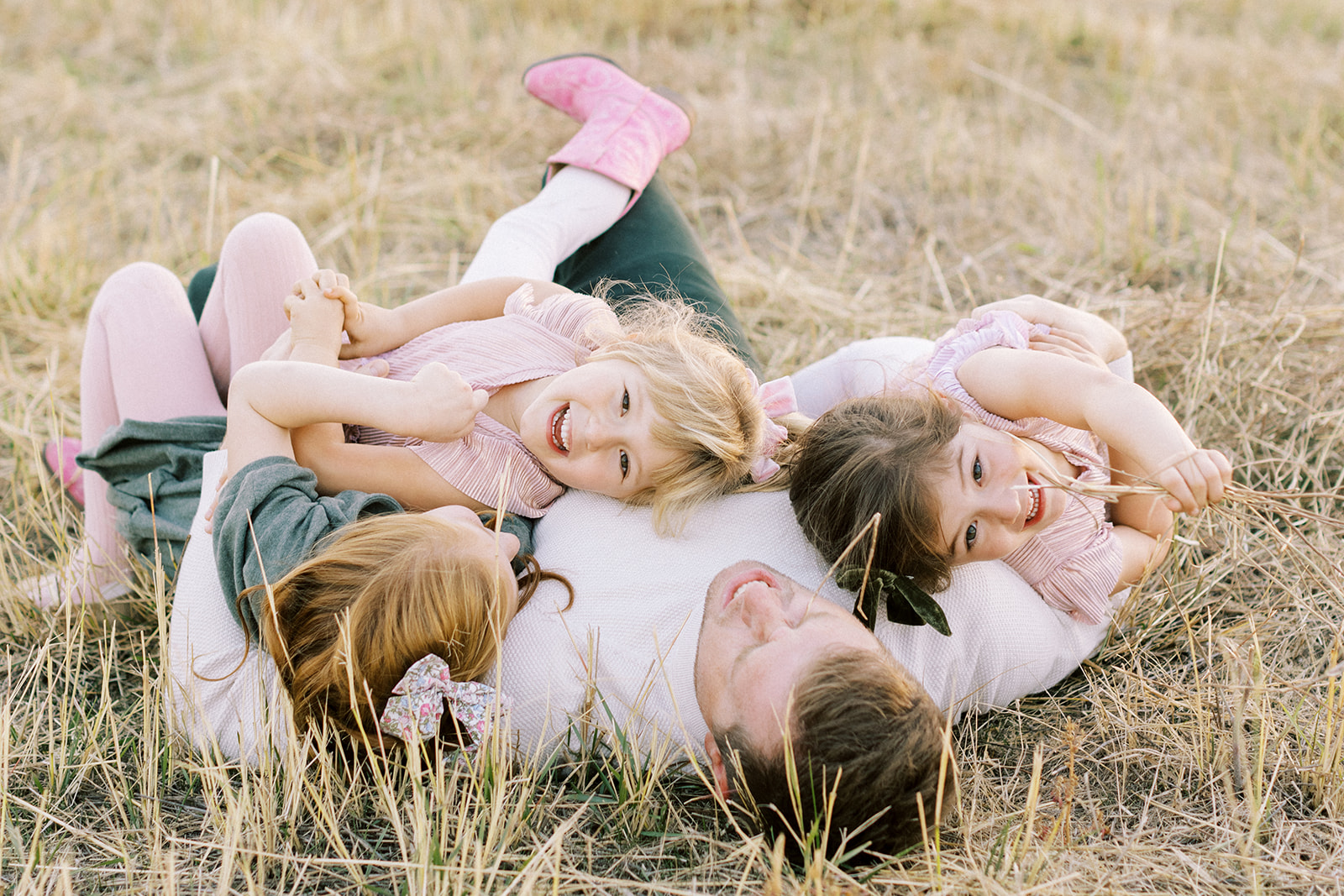 Father with three daughters snuggling in field at sunset in Spokane, Washington.