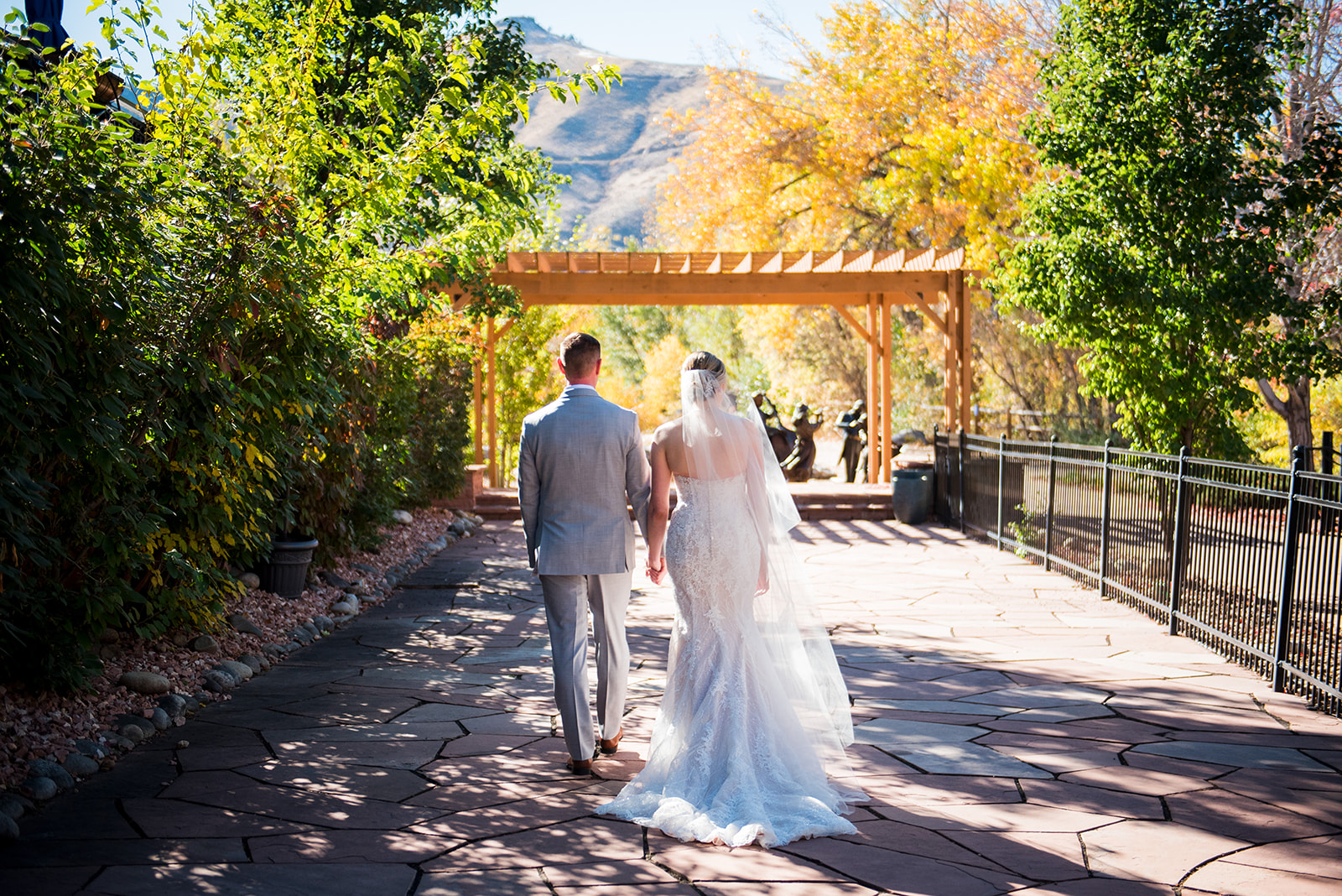 Bride and groom walk hand in hand away from the camera toward a stunning view of fall foilage.