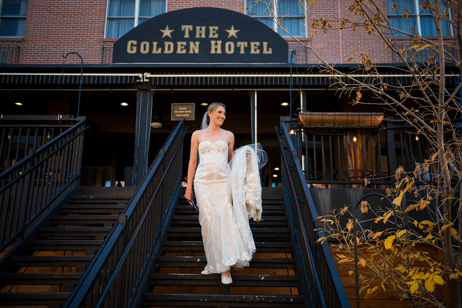 The bride walks down the front steps of The Golden Hotel in Colorado, holding the train of her dress in one hand.