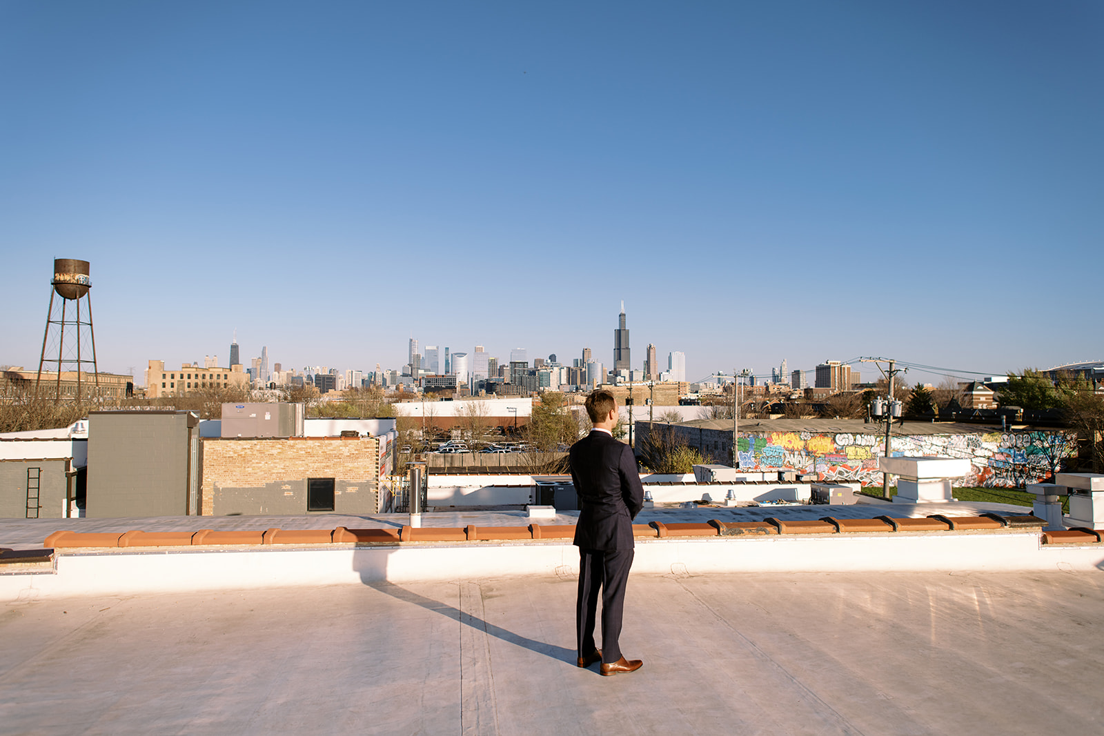 Groom waits for bride on rooftop of Walden Chicago with the Chicago skyline in the background