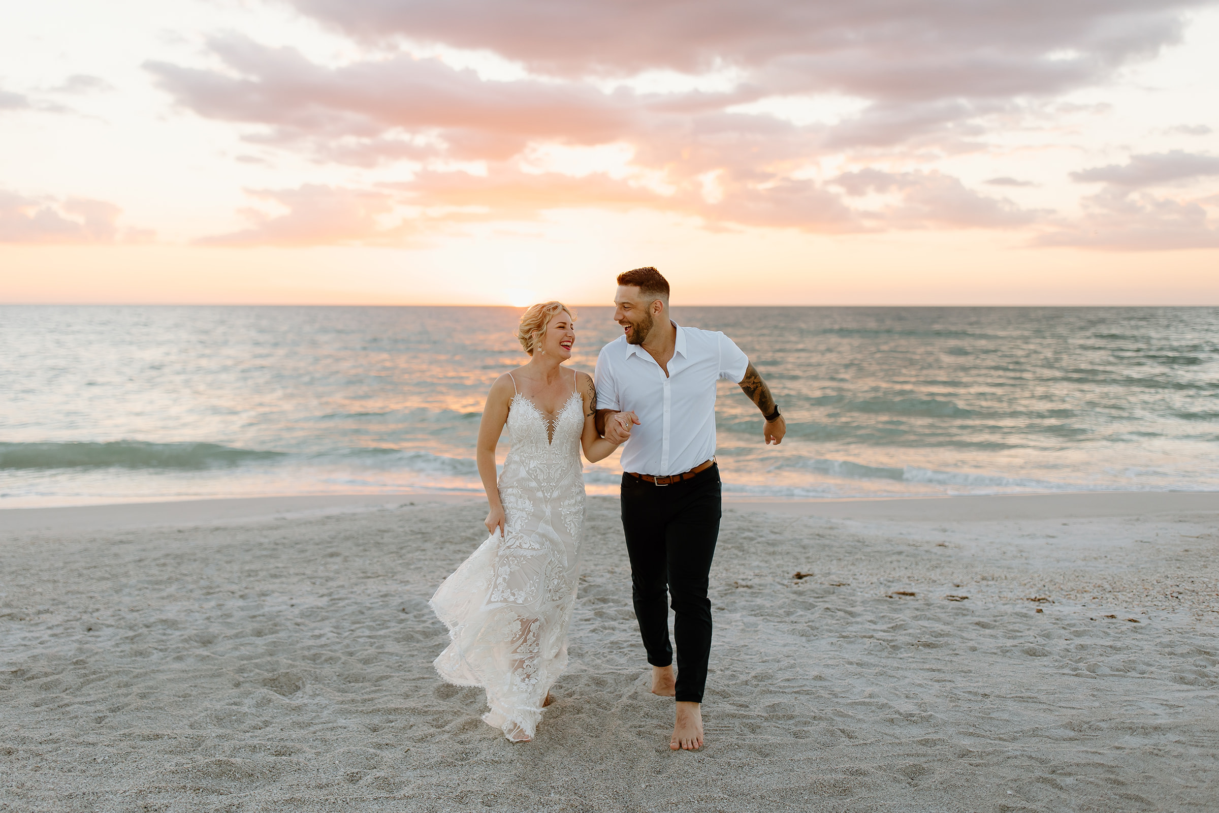 Bride and groom running towards the camera on the beach with a sunset in the background