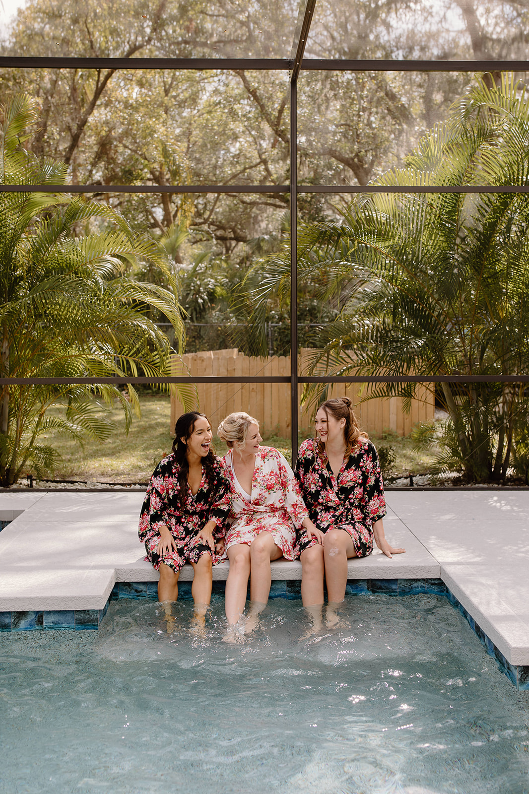 Bride and bridesmaids laughing in their matching floral robes while splashing water in the pool