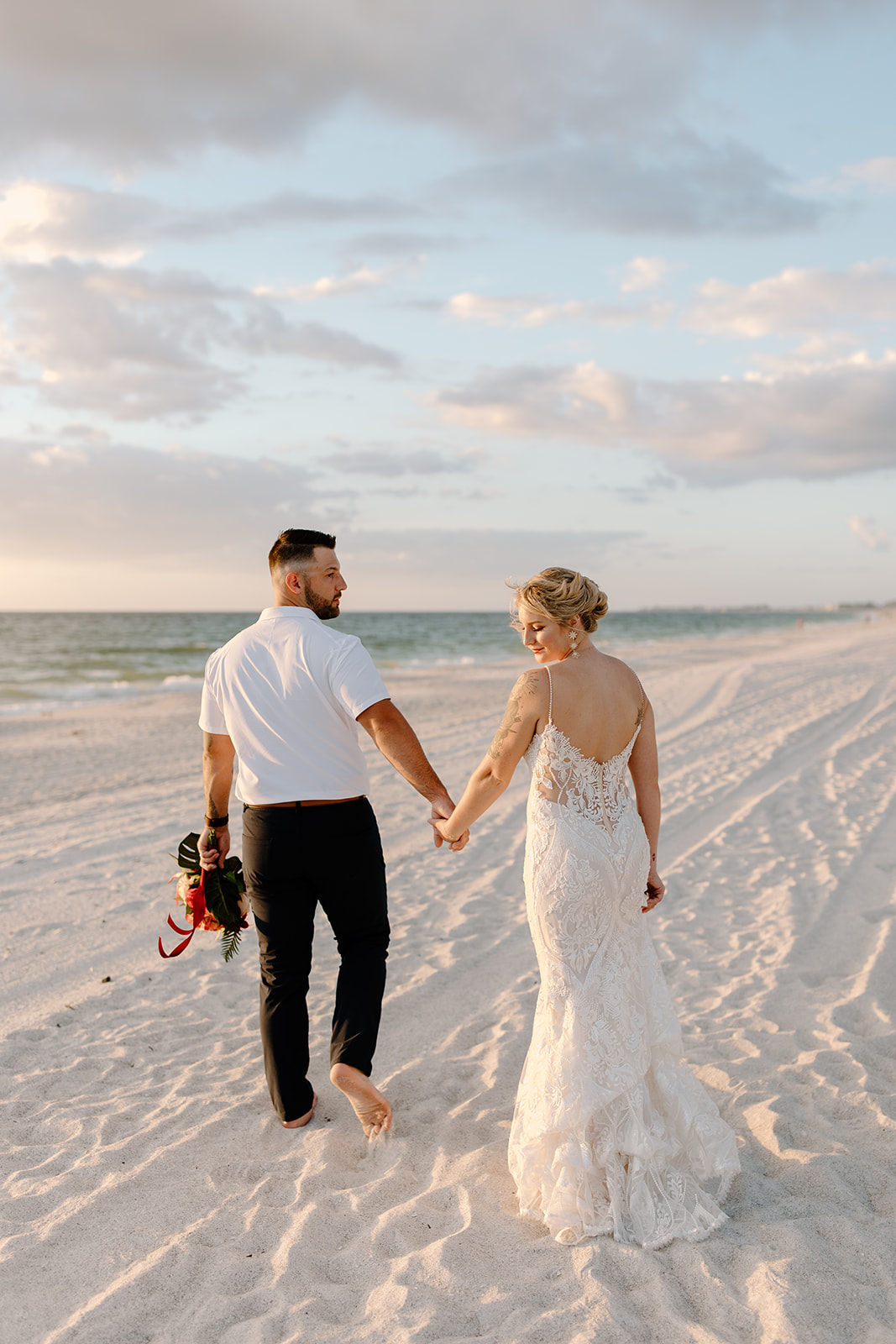 Bride and groom hold hands and walk along the beach