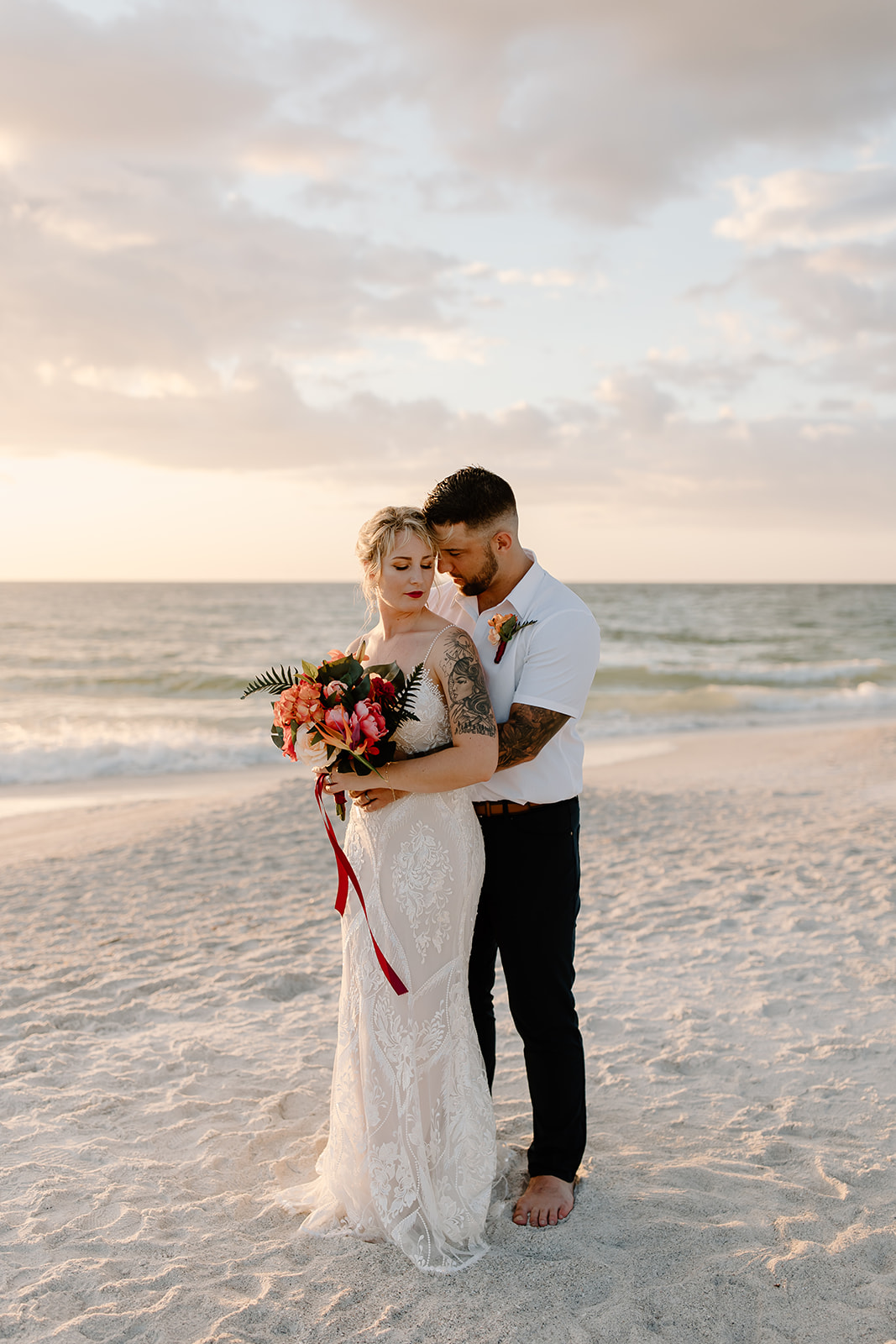 Groom hugs around his bride on the beach in front of the sunset