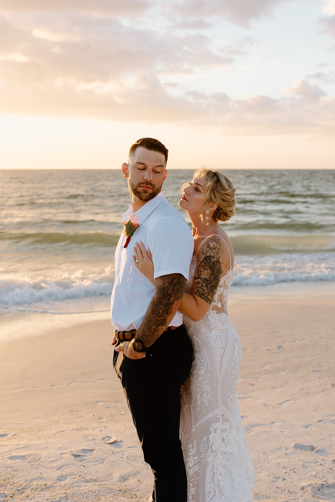 Bride hugs around her groom on the beach in front of the sunset