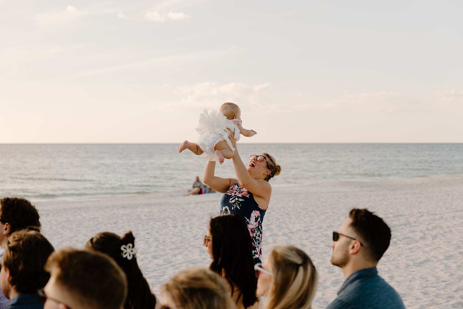 A woman tosses her daughter into the air with the ocean in the background