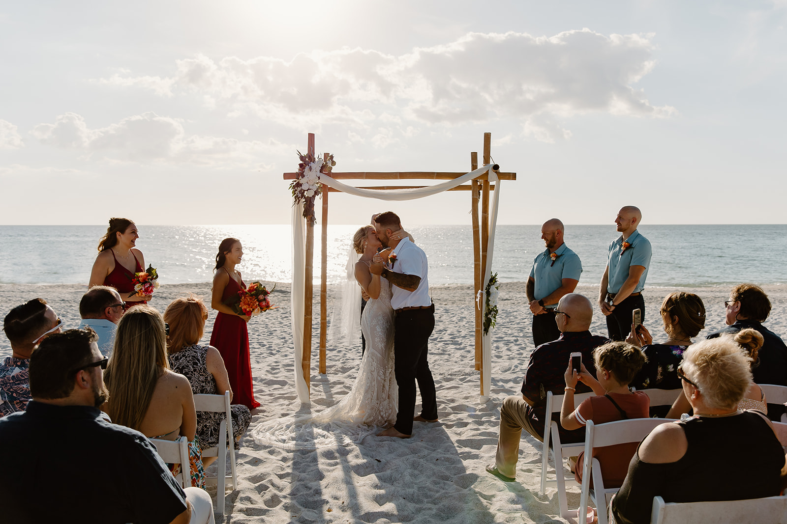 Bride and groom kiss in front of the arch during their ceremony on the beach