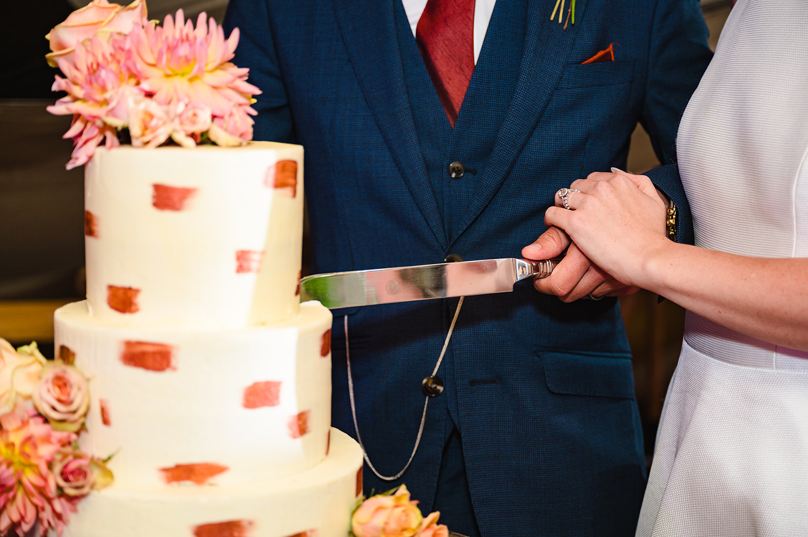 close up of bride and groom cutting their wedding cake with cream buttercream and terracotta accents