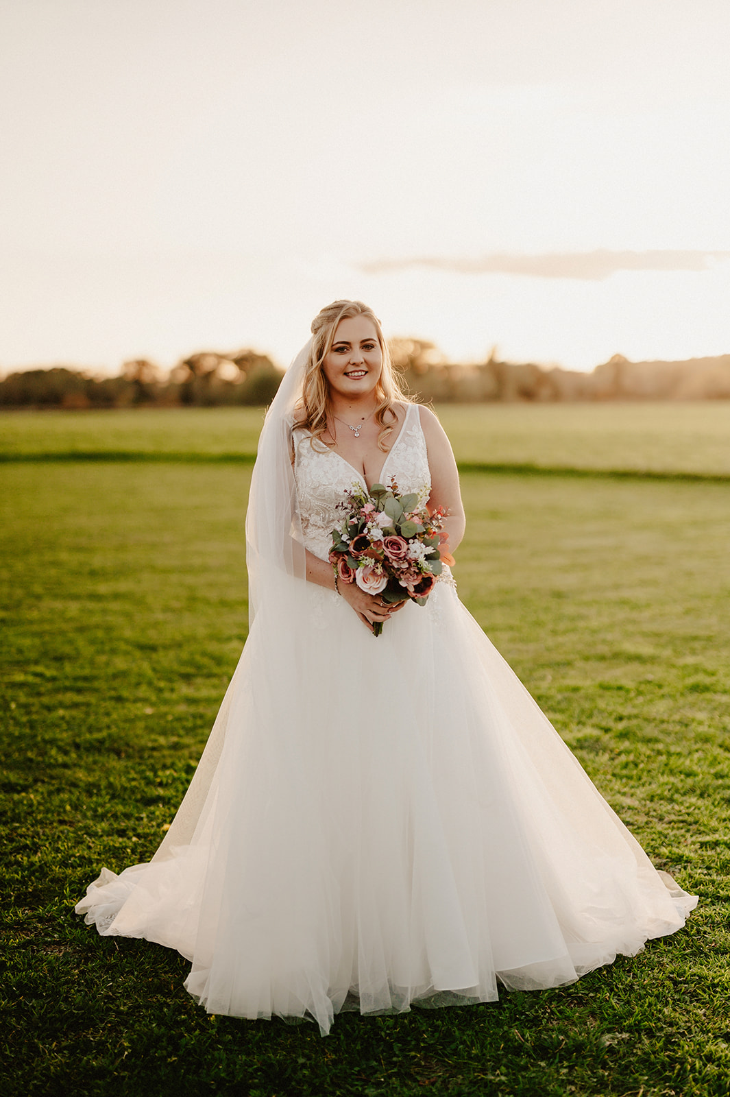 bride smiling in full length portrait wearing her white dress during golden hour at pentney abbey