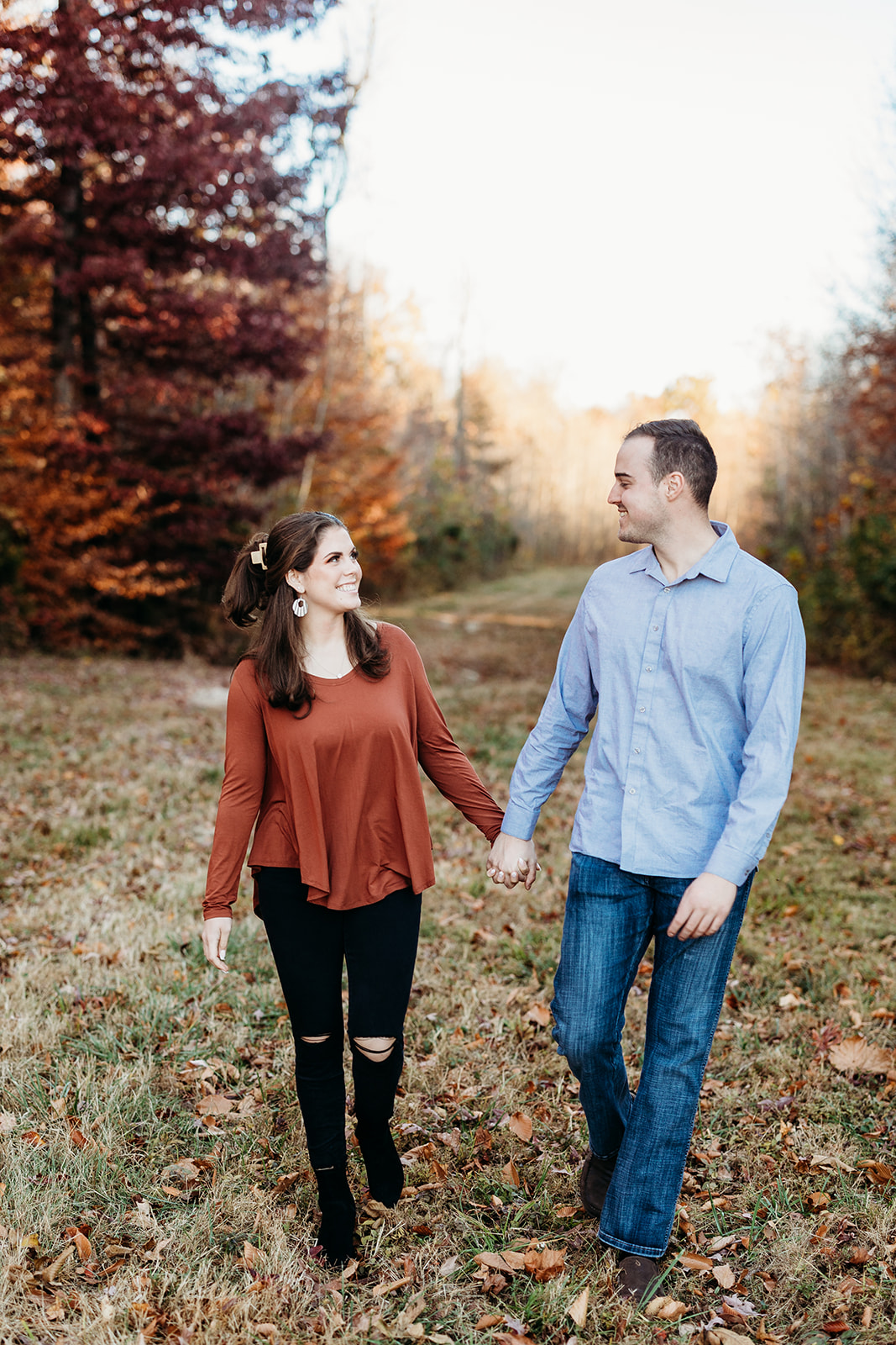 engaged couple walk hand in hand through fall leaves