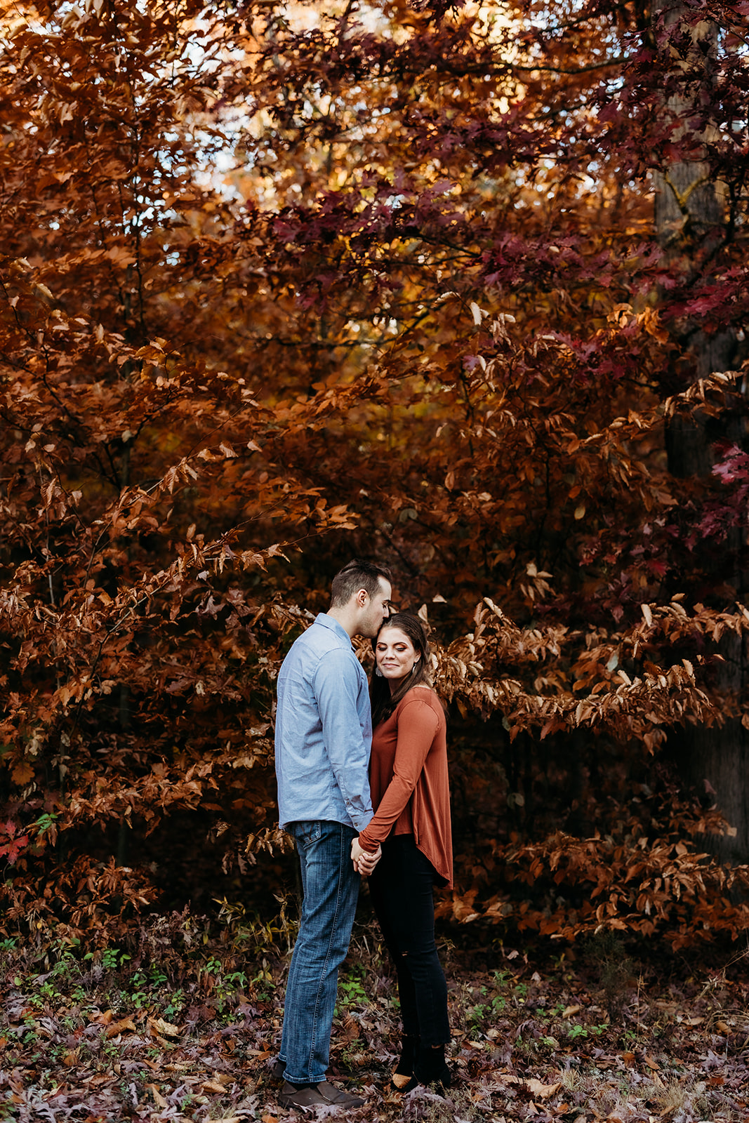 an engaged couple stands in front of beautiful fall leaves
