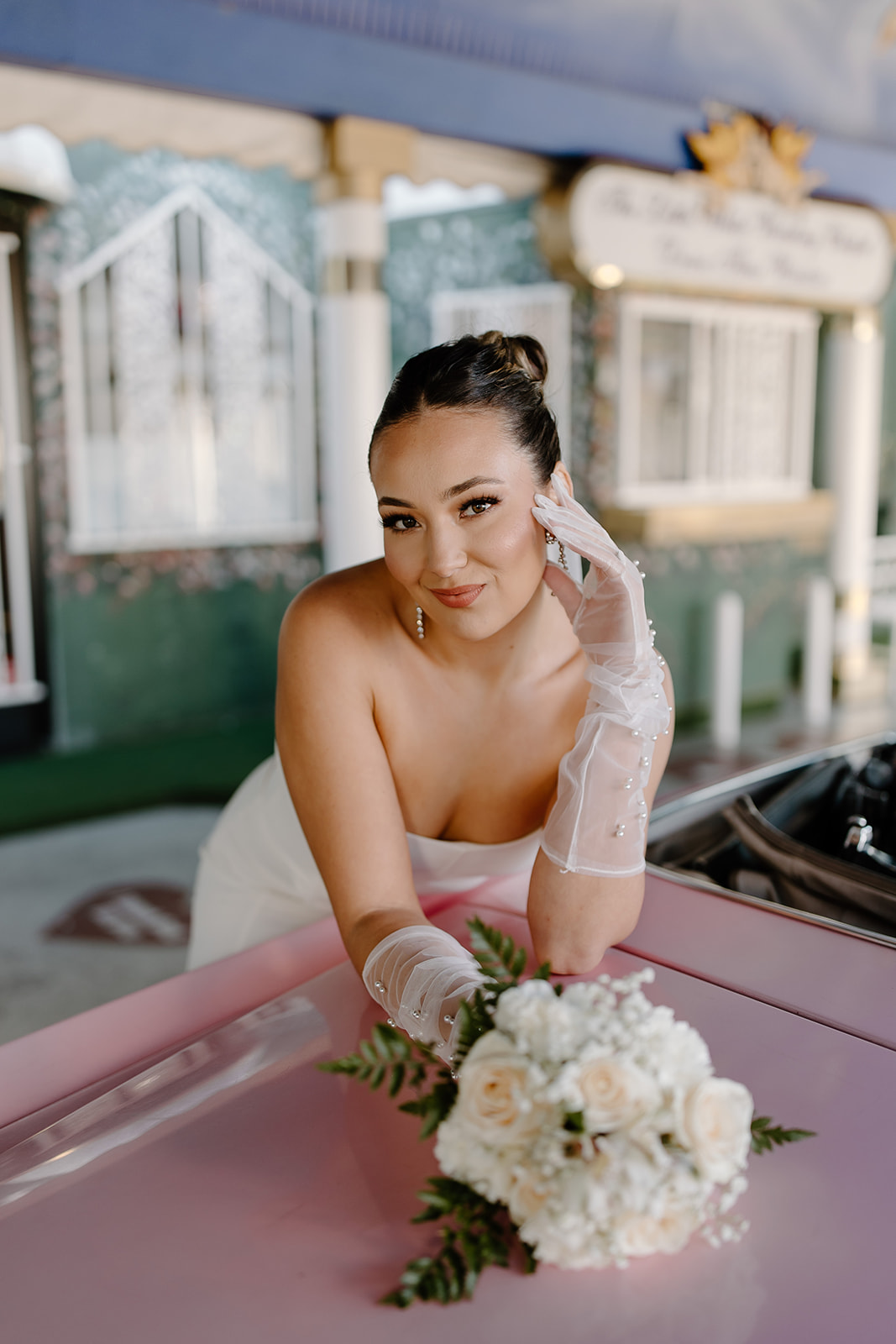 Bride leans onto a pink convertible