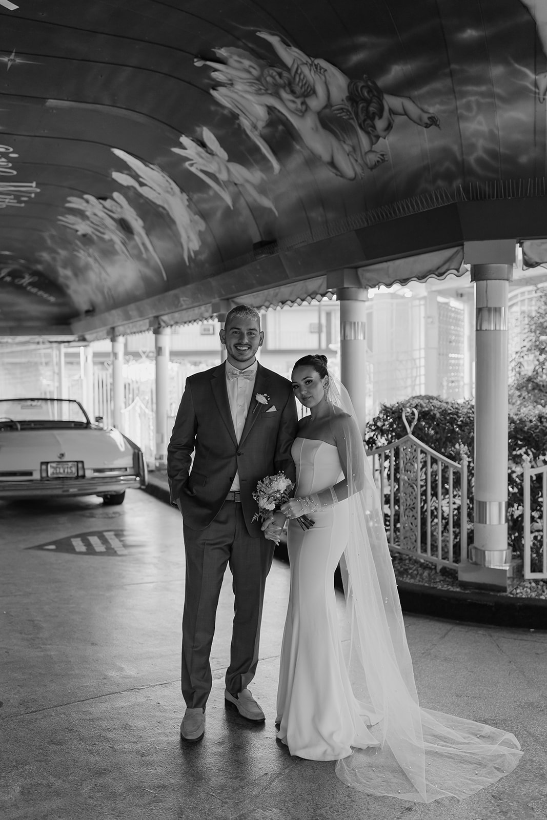 Bride and groom pose in front of a convertible